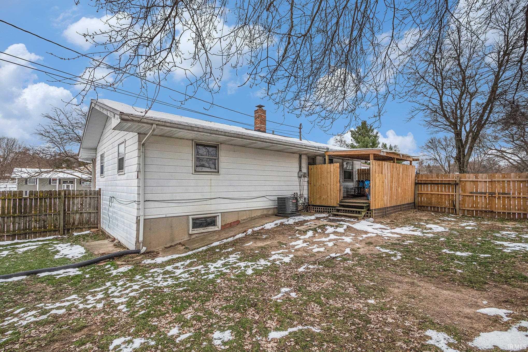 Snow covered rear of property with a fenced backyard and a chimney