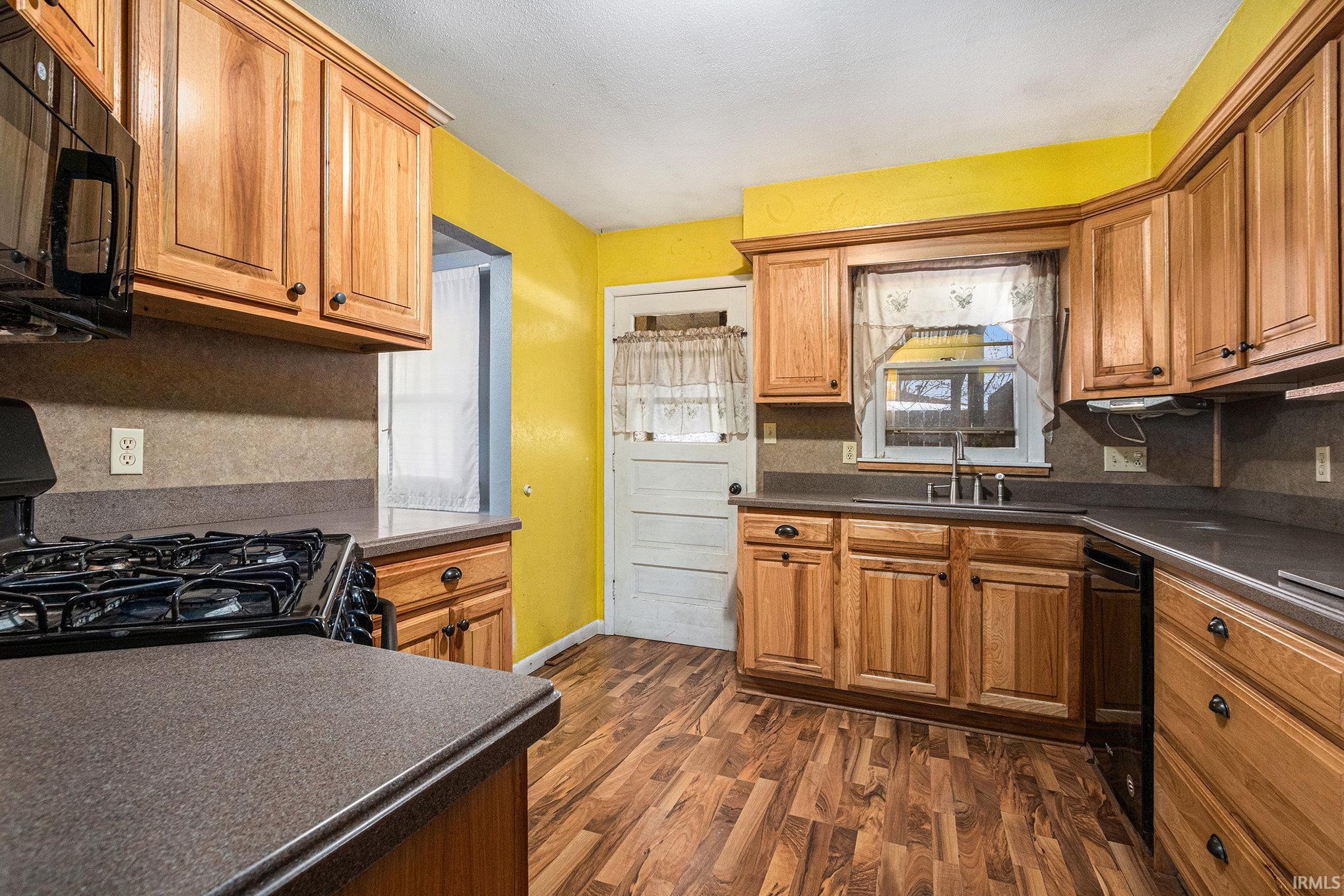 Kitchen featuring black appliances, dark countertops, dark wood-style floors, and brown cabinetry