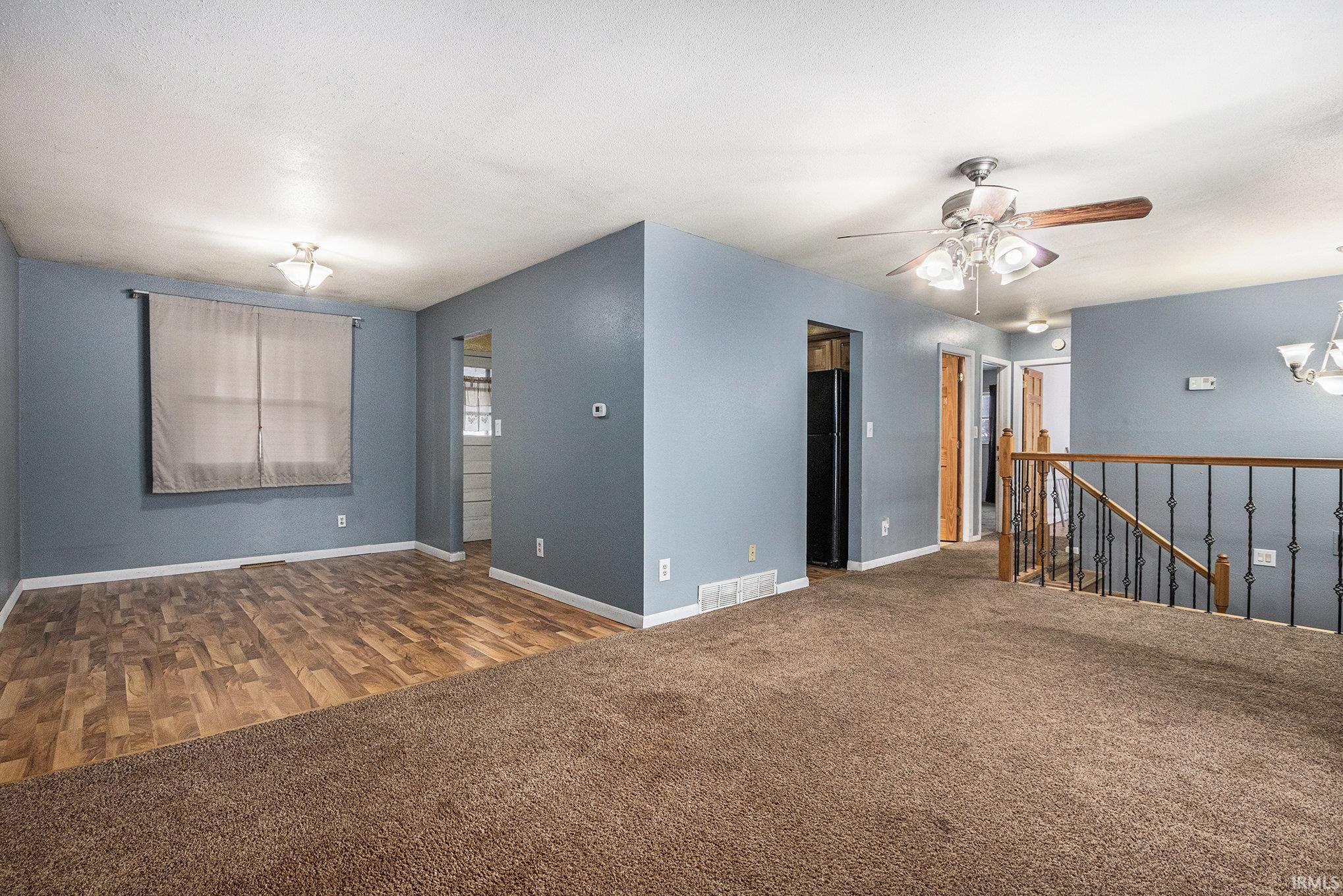 Carpeted spare room featuring wood finished floors, ceiling fan, and a chandelier