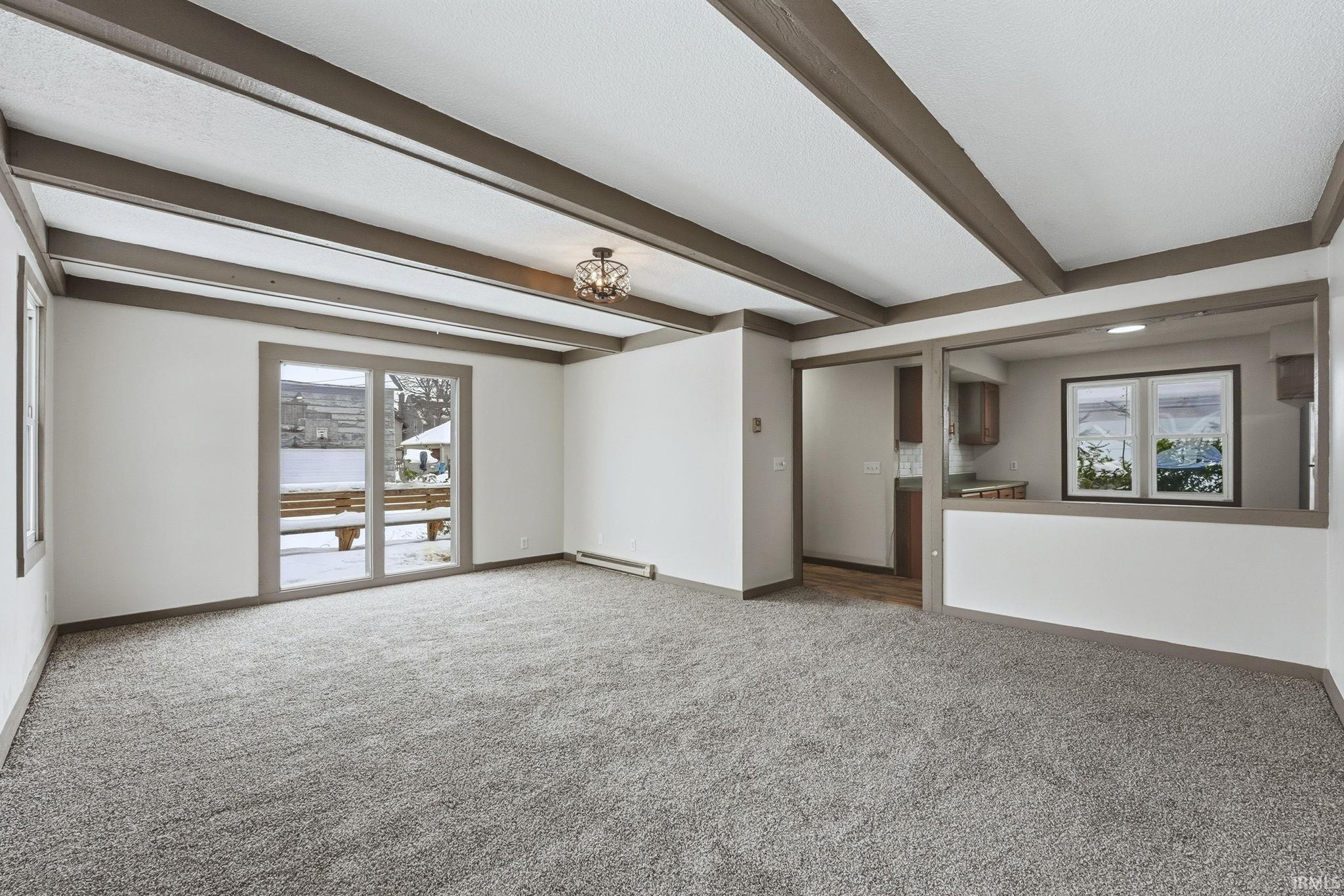 Unfurnished living room featuring beamed ceiling, healthy amount of natural light, carpet, a chandelier, and a baseboard radiator