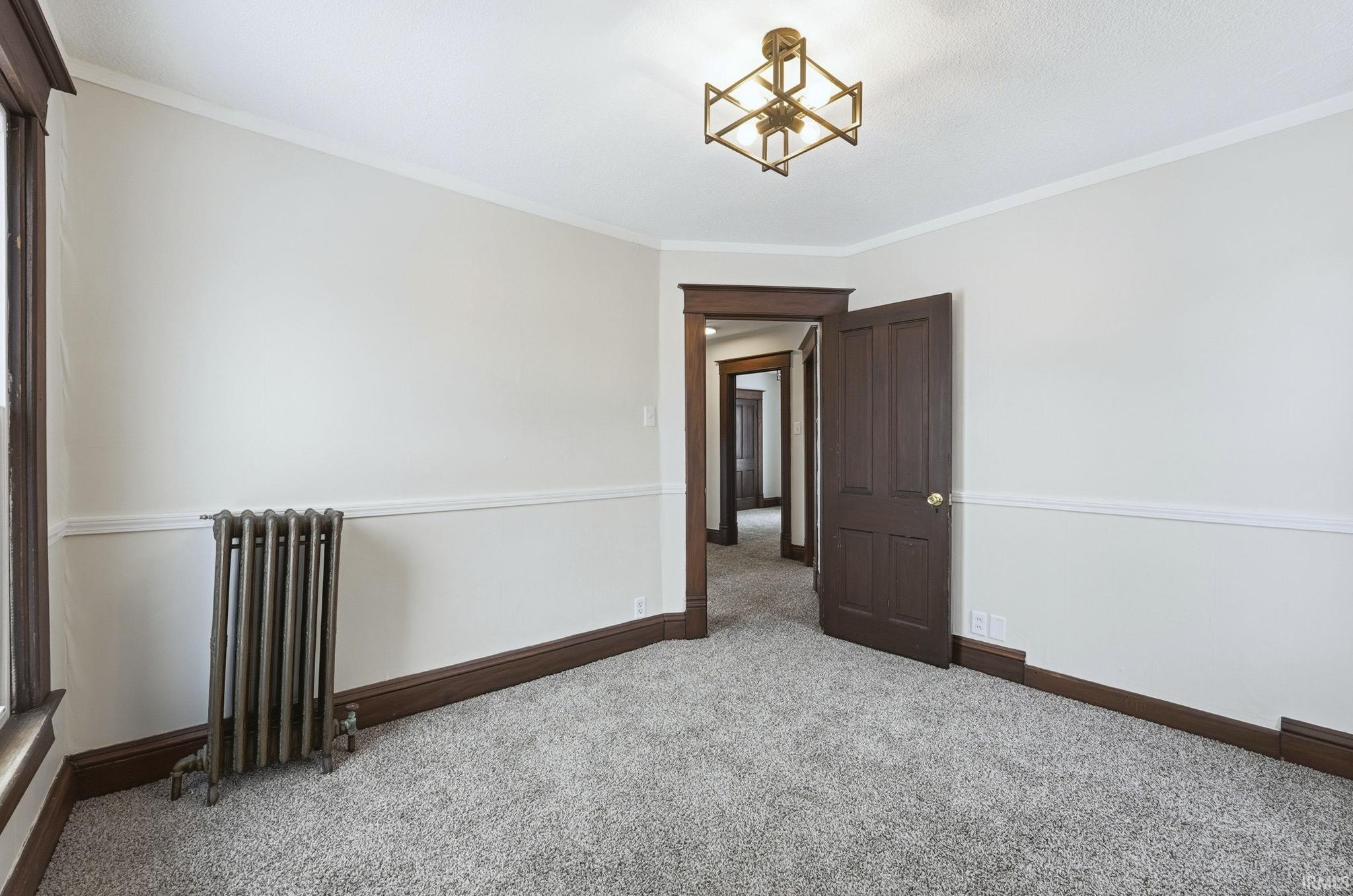 Carpeted spare room featuring radiator heating unit and ornamental molding