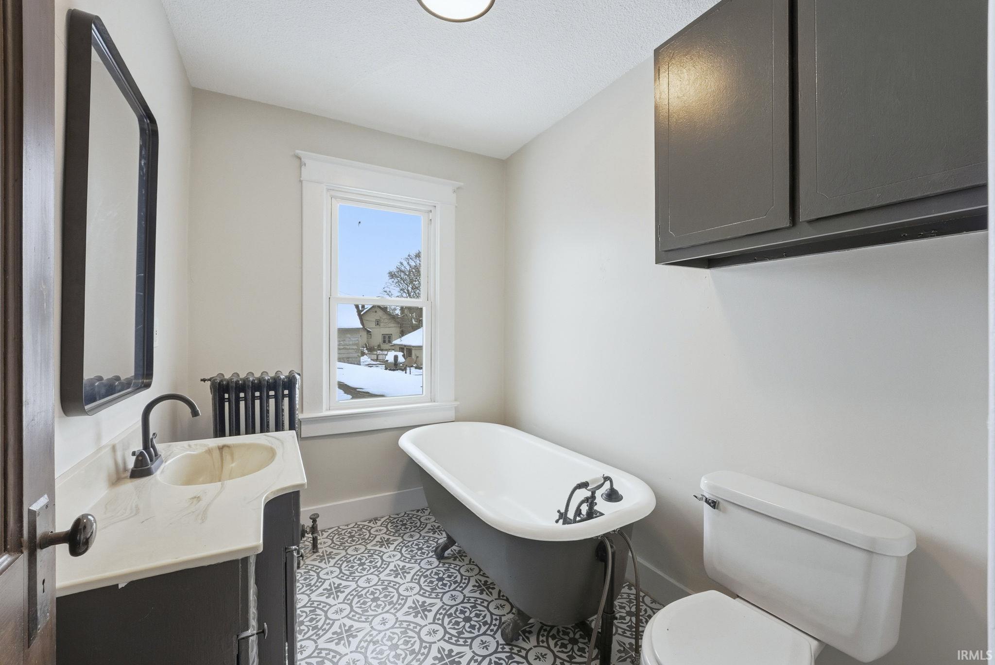 Bathroom with a freestanding bath, vanity, radiator heating unit, and light tile patterned floors