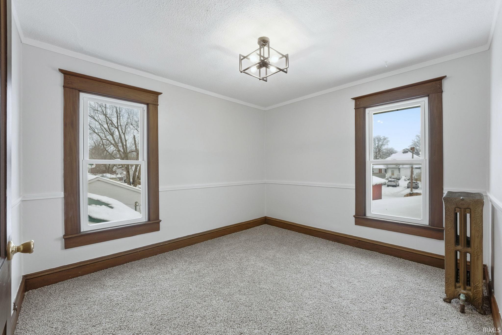 Unfurnished room featuring radiator heating unit, carpet floors, ornamental molding, a chandelier, and a textured ceiling