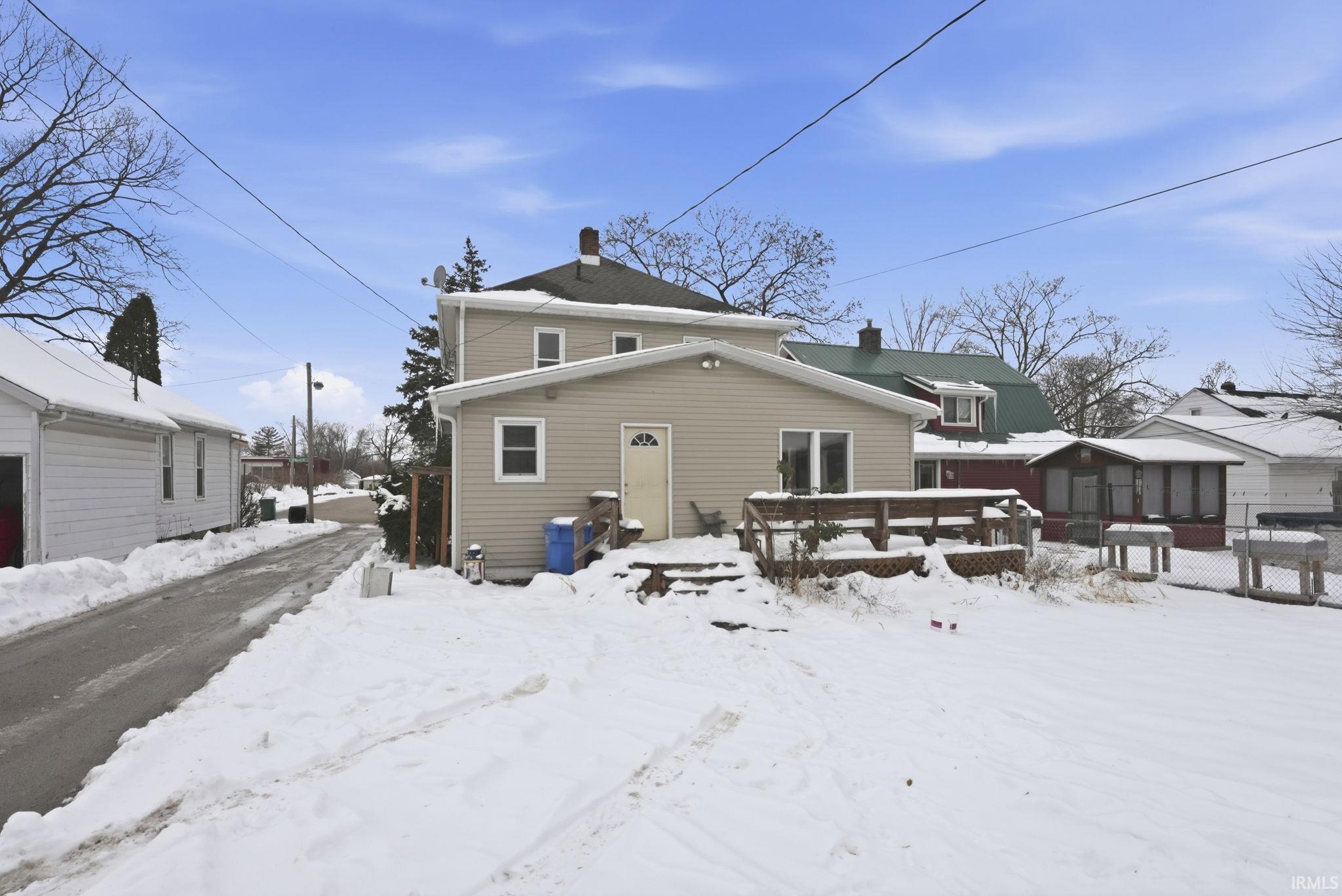 Snow covered back of property featuring a chimney and a deck