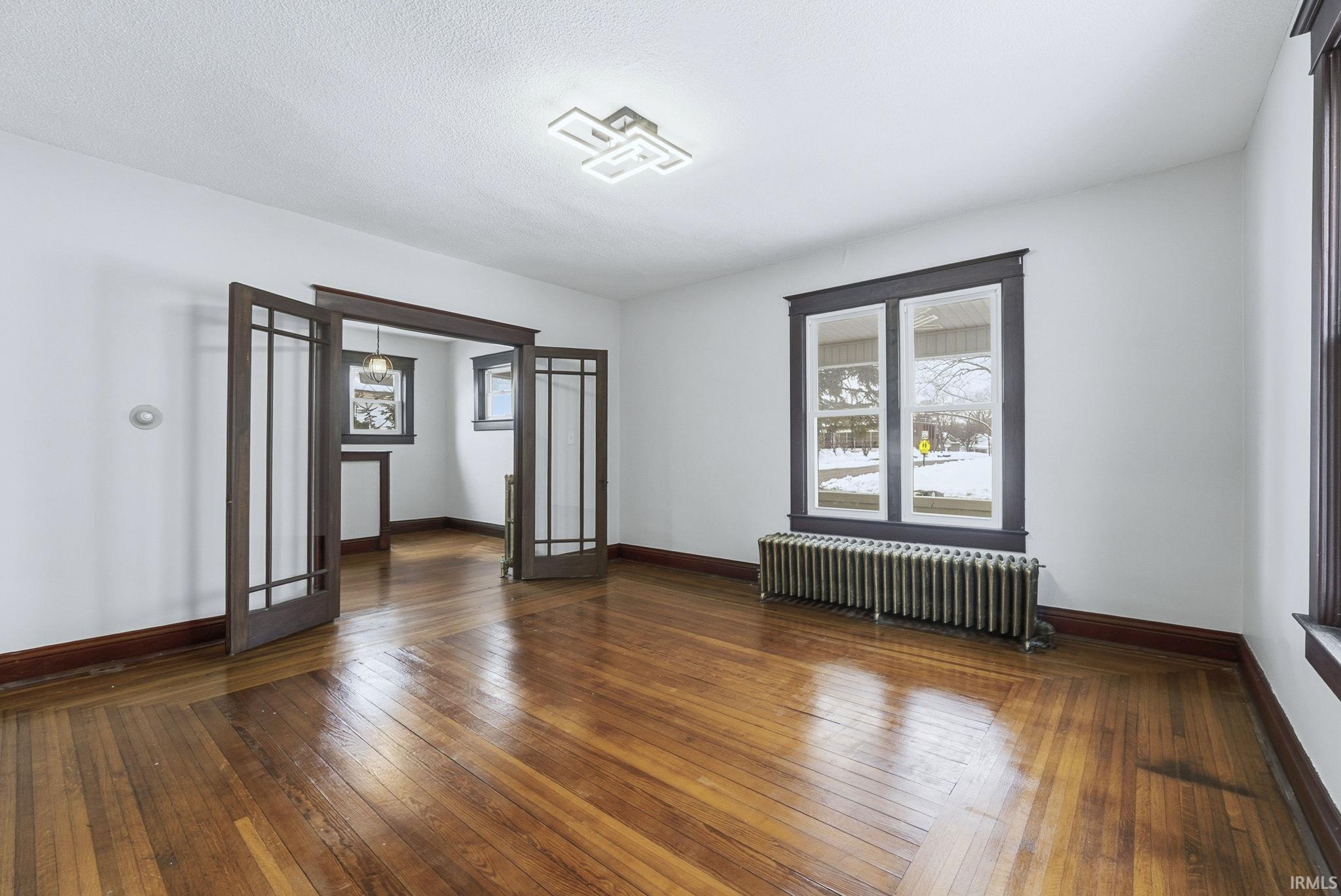 Spare room with radiator heating unit, hardwood / wood-style floors, french doors, and a textured ceiling