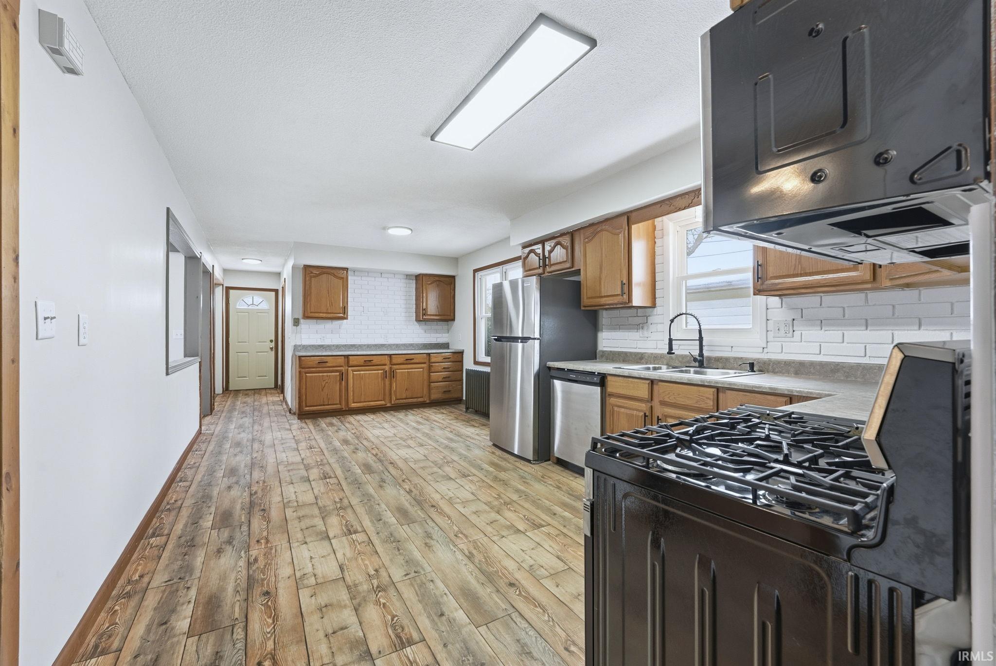 Kitchen with appliances with stainless steel finishes, light wood-type flooring, brown cabinetry, and light countertops