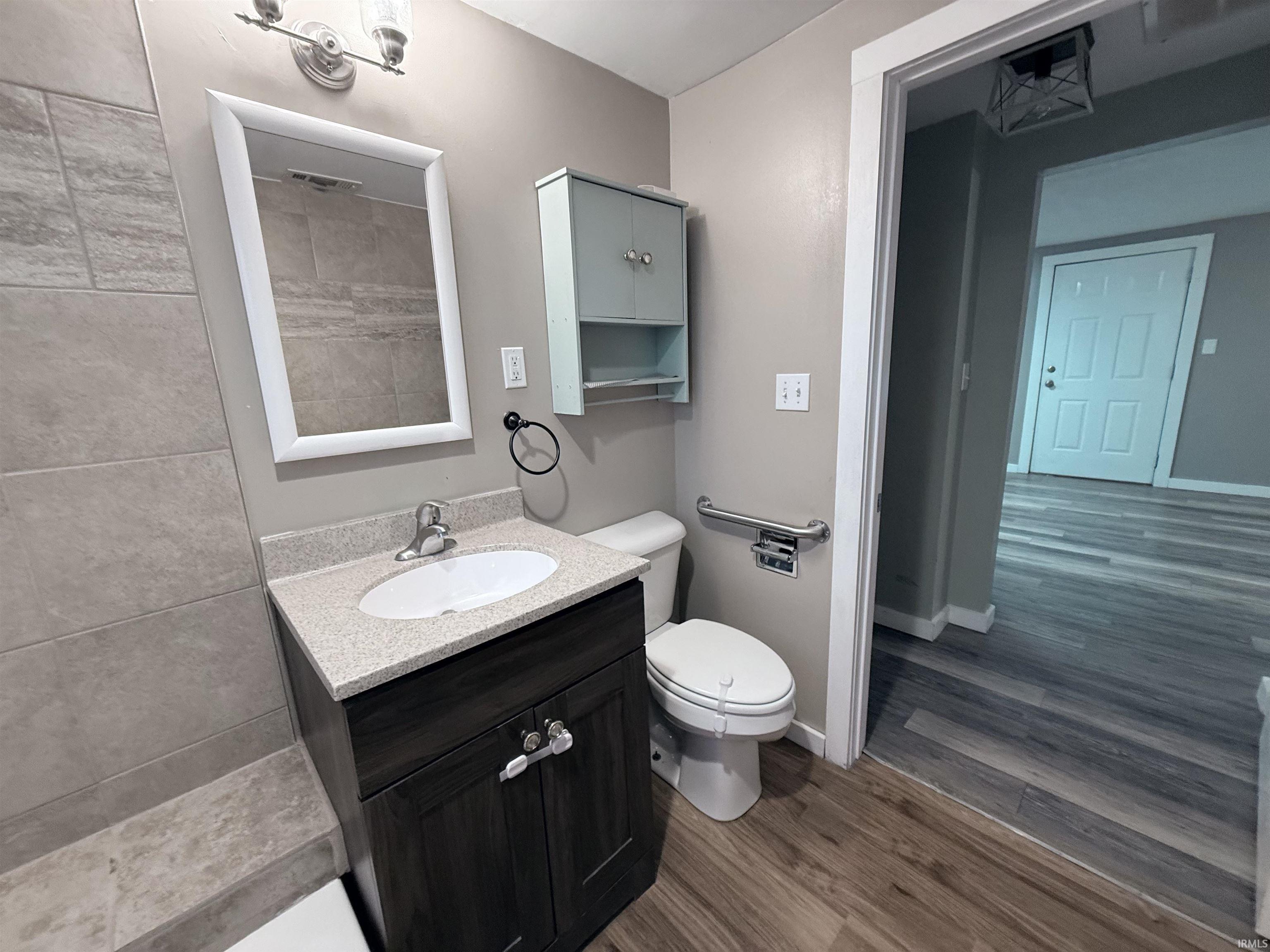 Bathroom with vanity, tiled shower, and dark wood-style floors