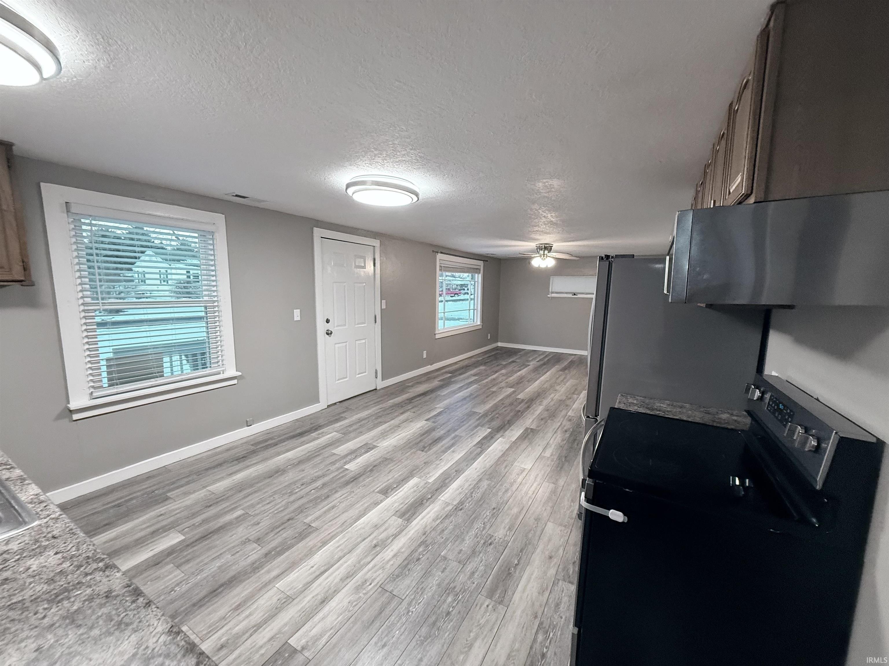 Kitchen with black range with electric cooktop, a textured ceiling, range hood, light wood finished floors, and light countertops