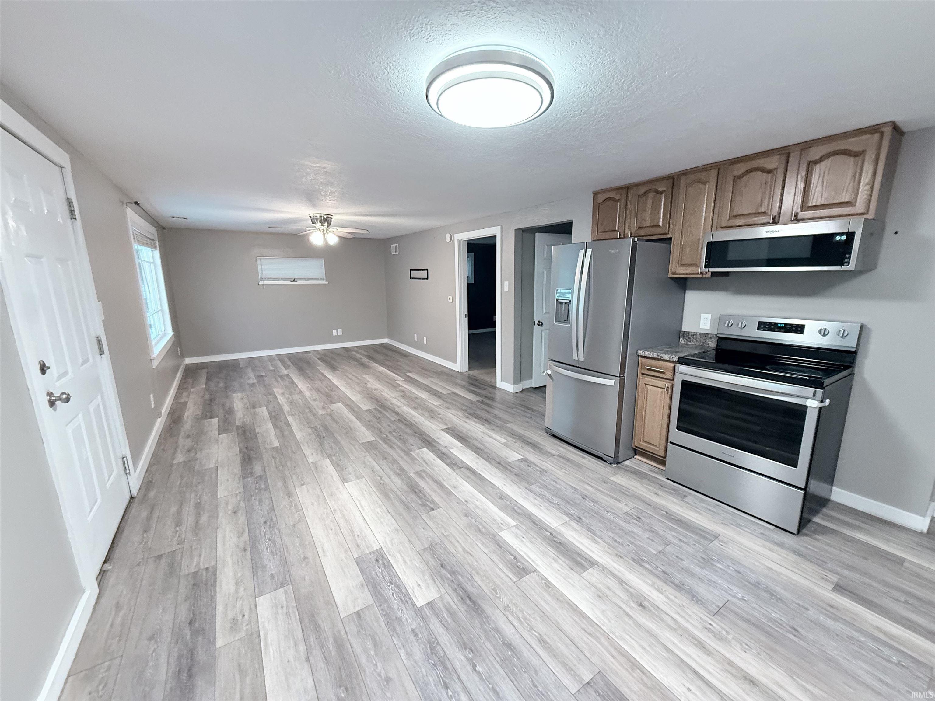 Kitchen with appliances with stainless steel finishes, ceiling fan, a textured ceiling, light wood-style flooring, and open floor plan