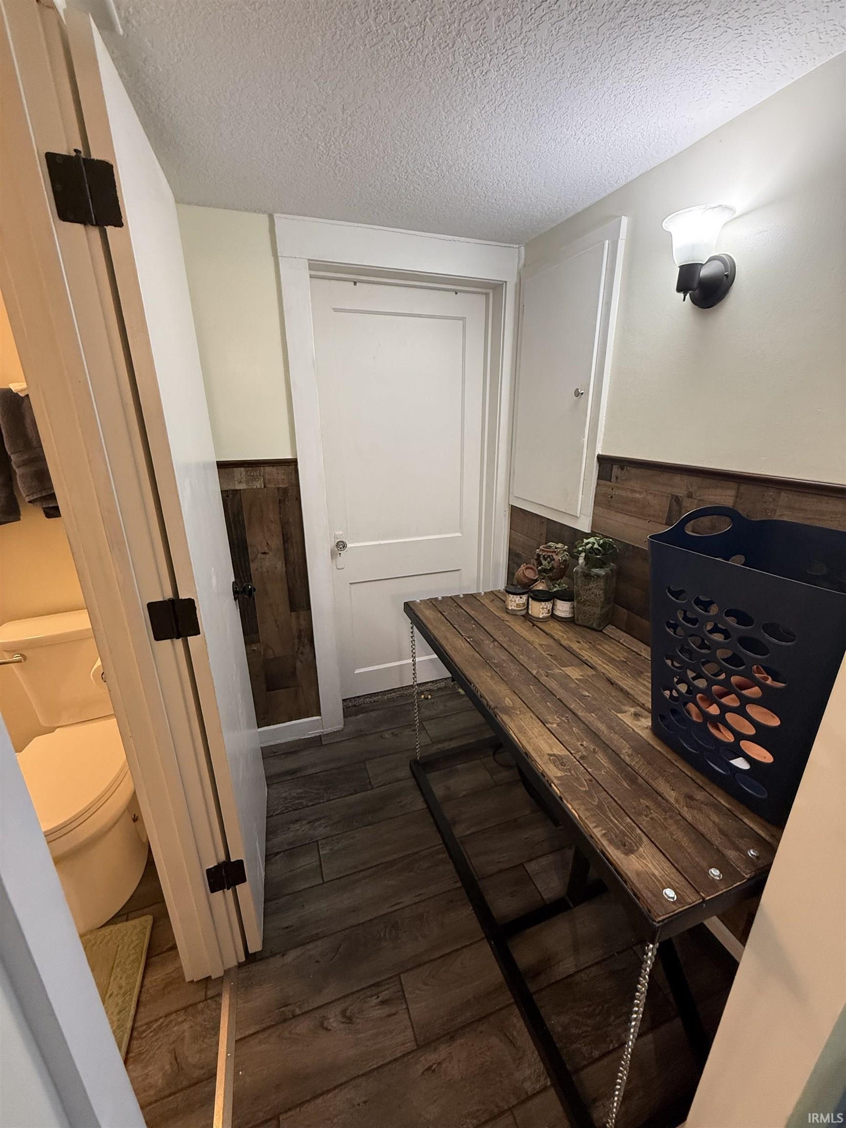 Interior space featuring wainscoting, dark wood-style flooring, a textured ceiling, and wood walls