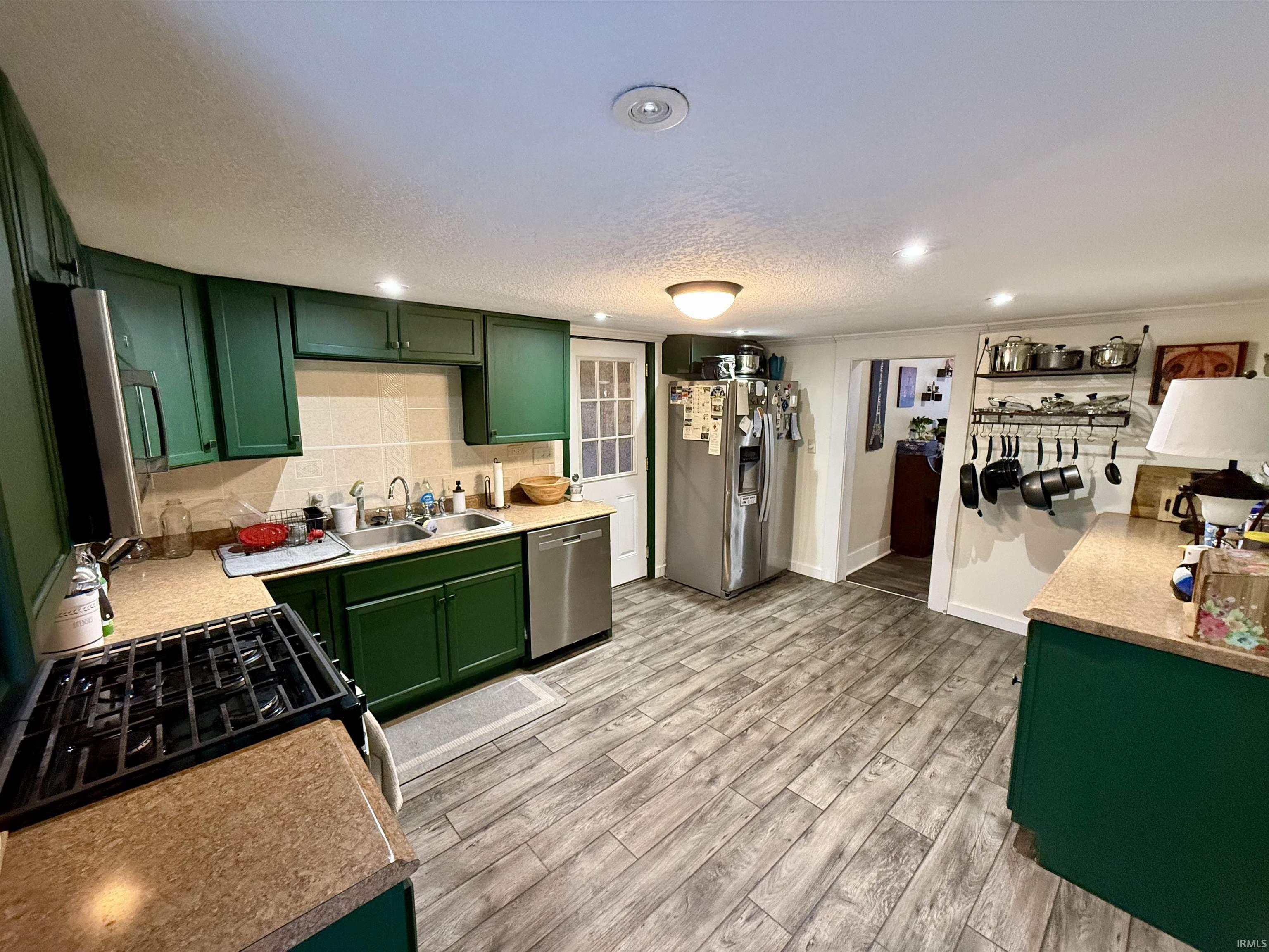 Kitchen with green cabinets, appliances with stainless steel finishes, wood tiled floors, light countertops, and a textured ceiling