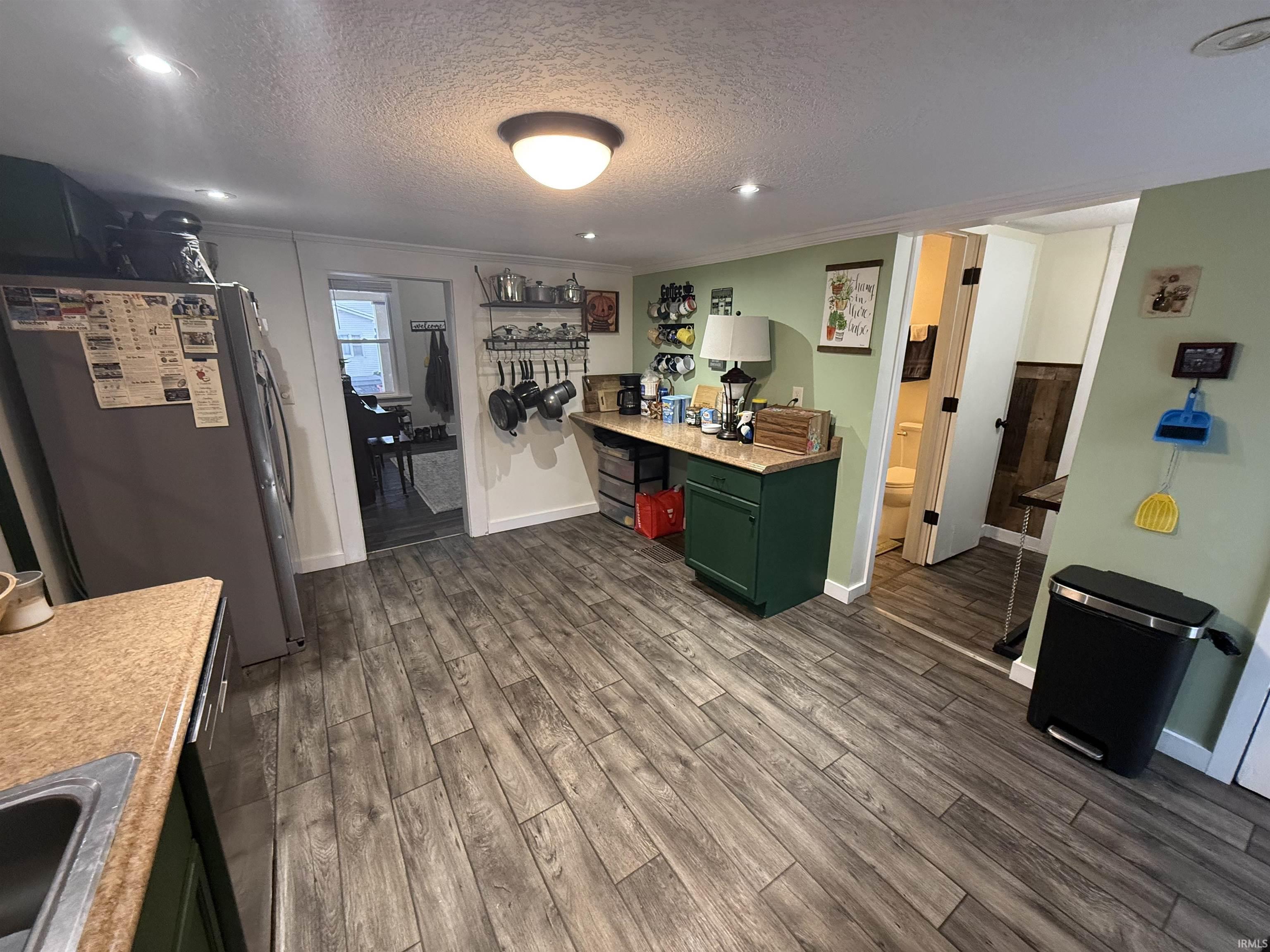 Kitchen with green cabinetry, freestanding refrigerator, a textured ceiling, light countertops, and dark wood-type flooring