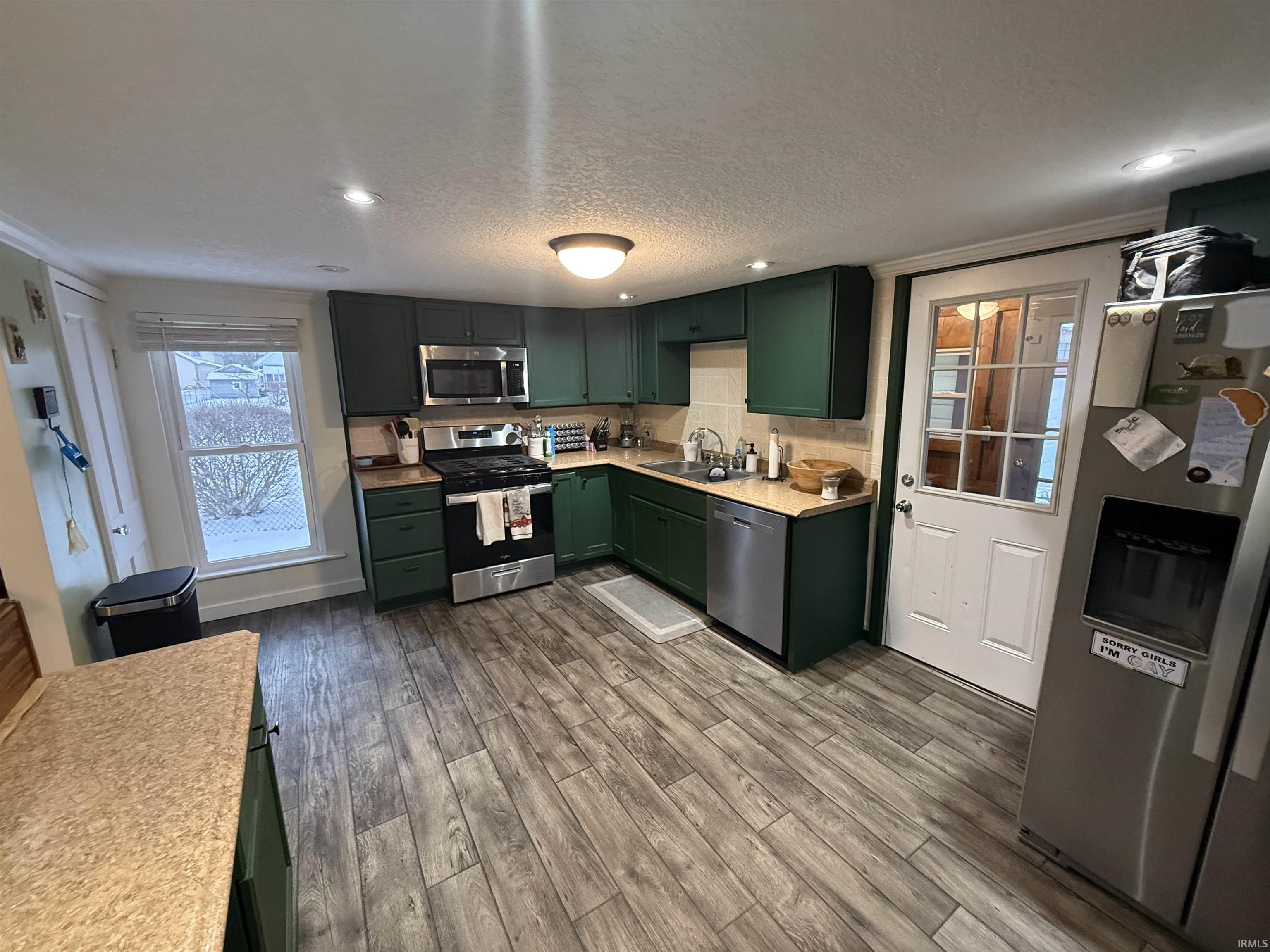 Kitchen featuring green cabinetry, appliances with stainless steel finishes, light countertops, recessed lighting, and dark wood-type flooring