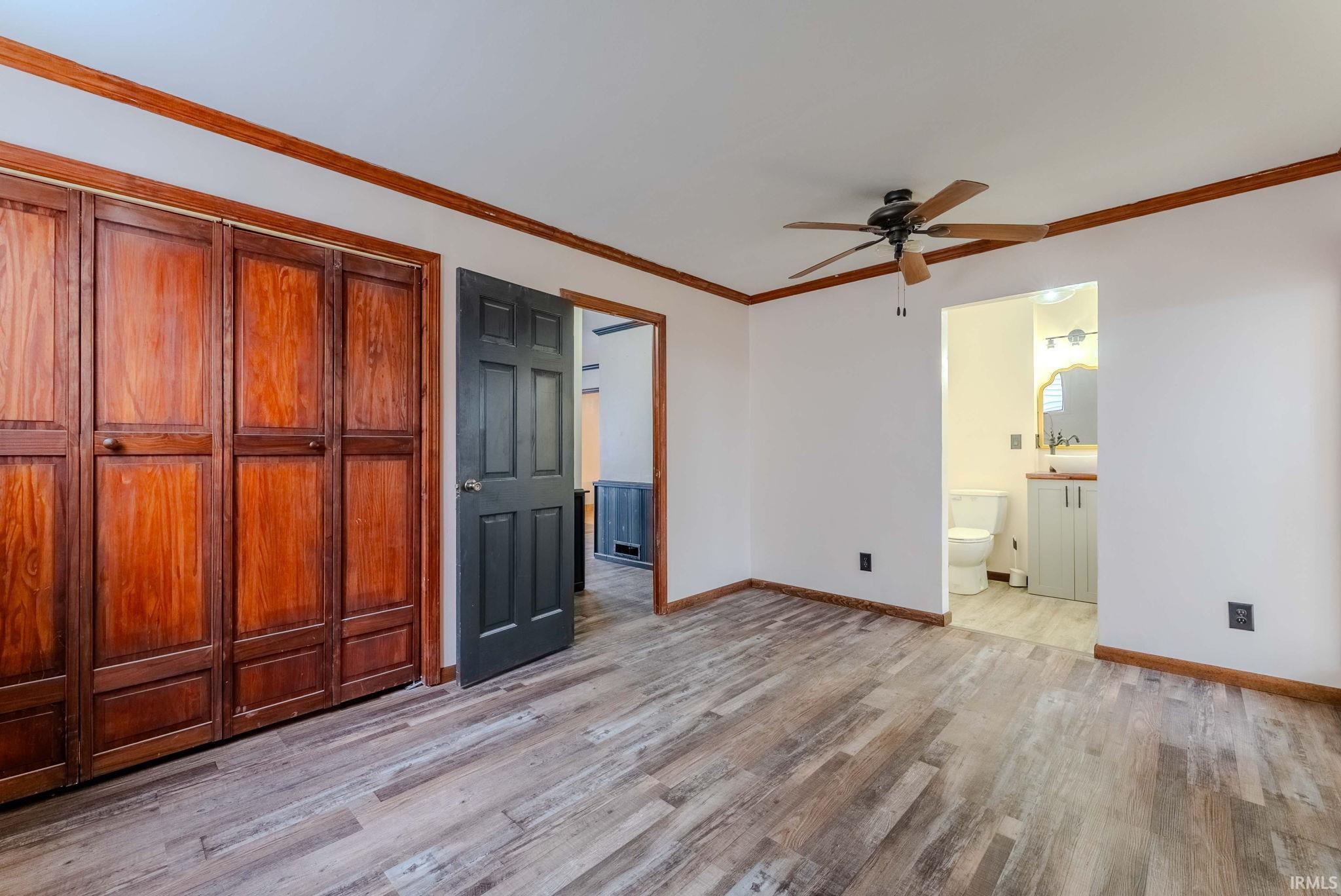 Unfurnished bedroom featuring a closet, crown molding, light wood finished floors, and a ceiling fan