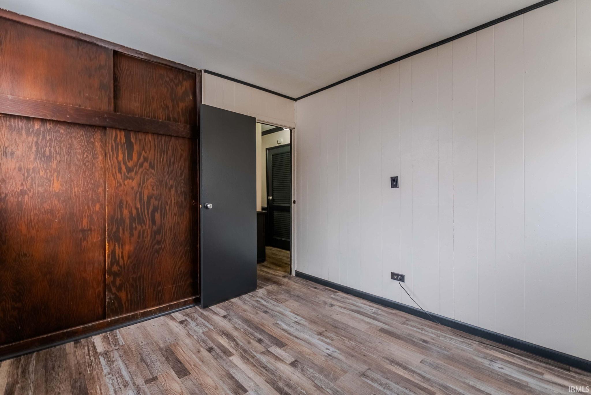 Unfurnished bedroom featuring light wood finished floors, a closet, and wooden walls