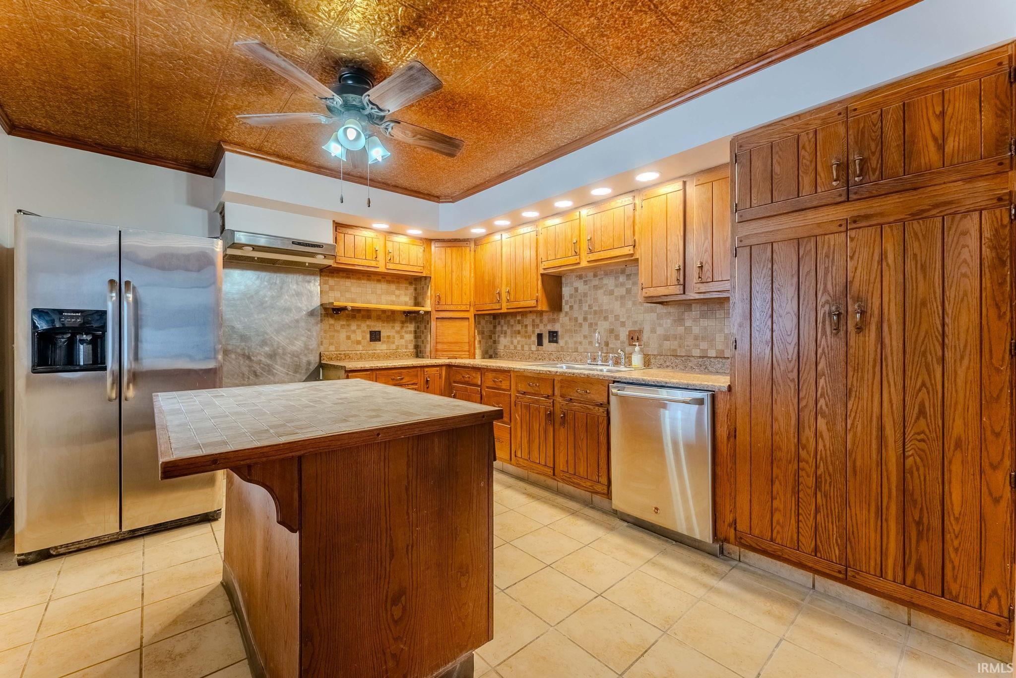 Kitchen with crown molding, appliances with stainless steel finishes, brown cabinetry, an ornate ceiling, and a ceiling fan