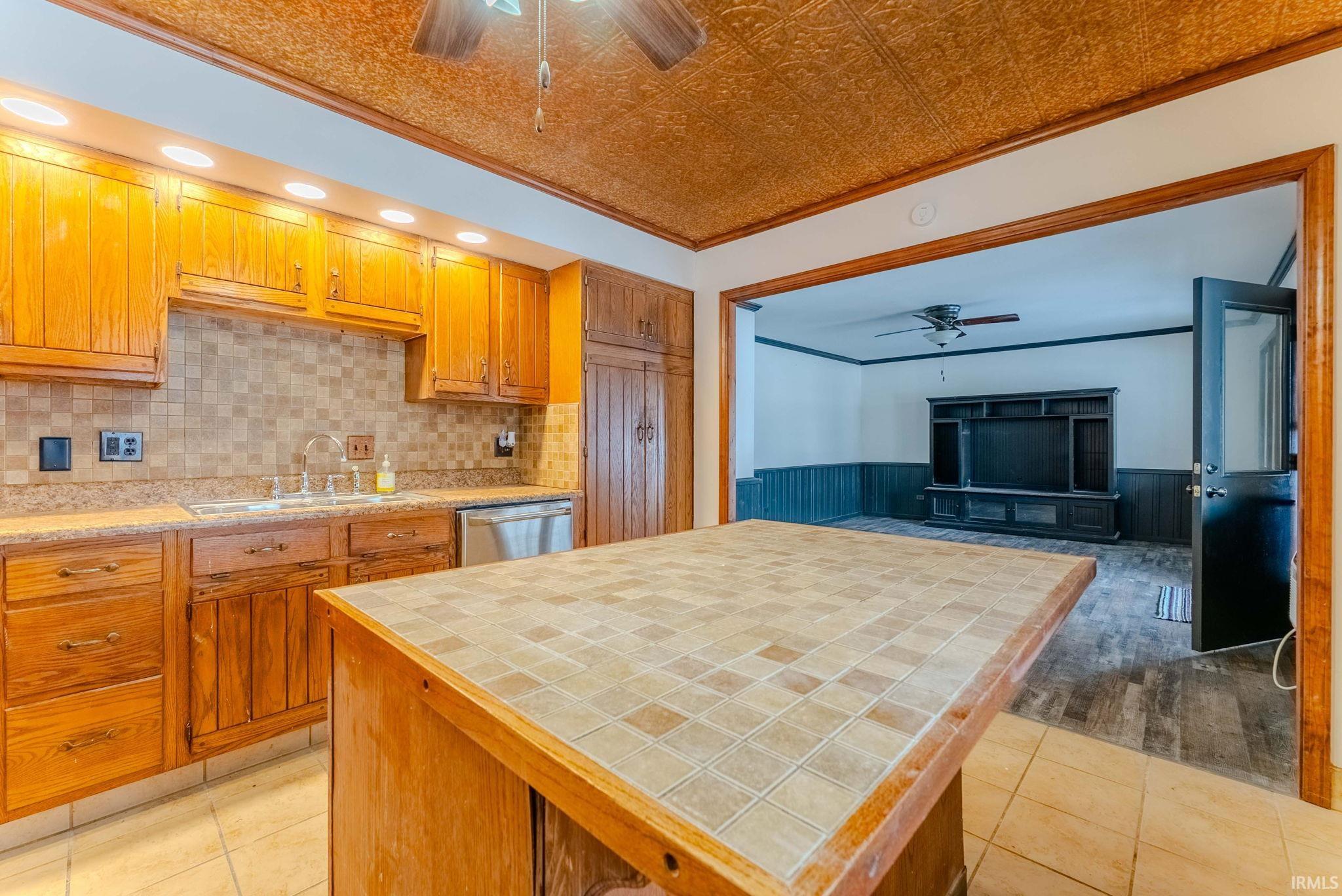Kitchen with ceiling fan, crown molding, an ornate ceiling, tile counters, and a wainscoted wall