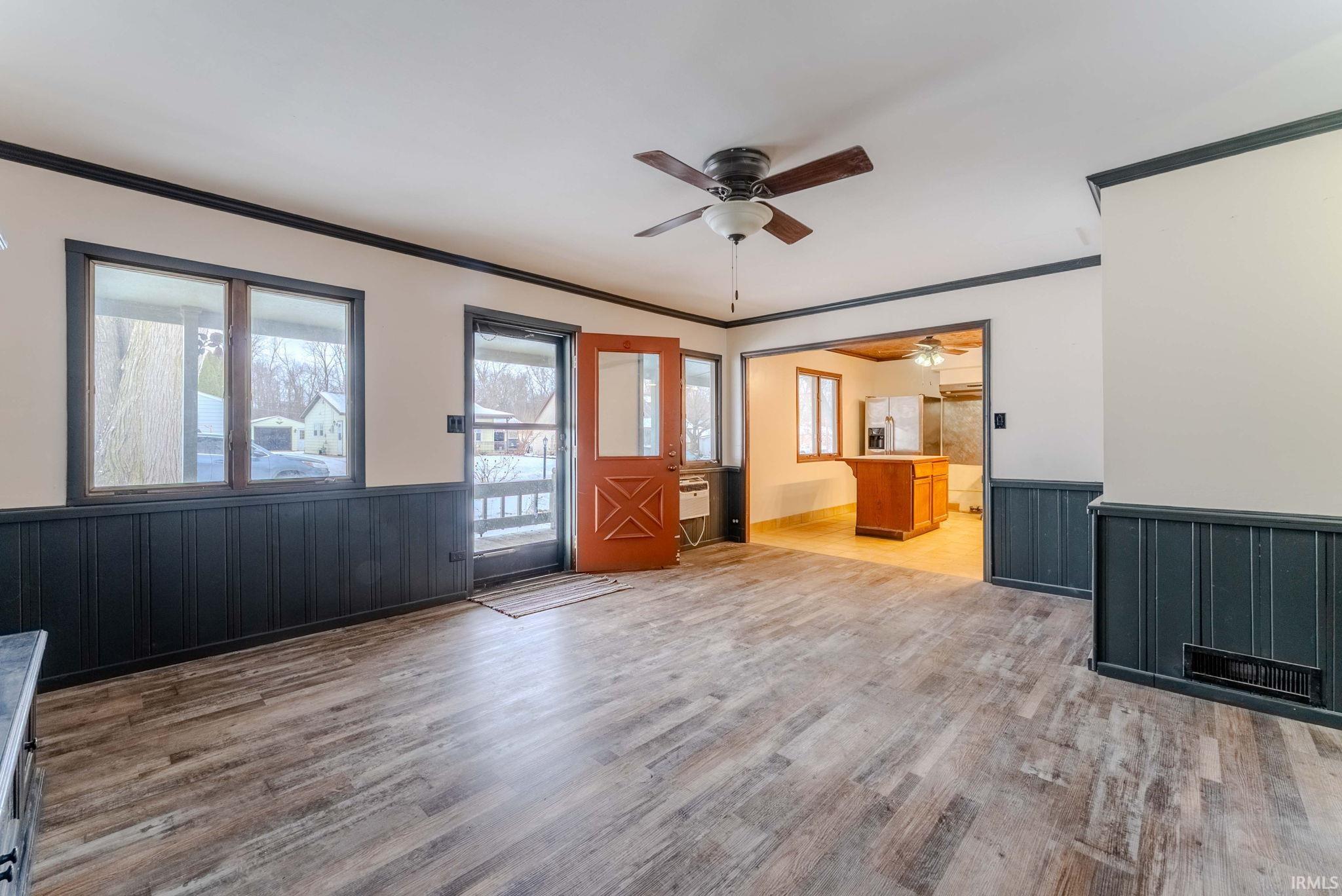 Unfurnished living room featuring wainscoting, ornamental molding, wood walls, light wood-type flooring, and ceiling fan