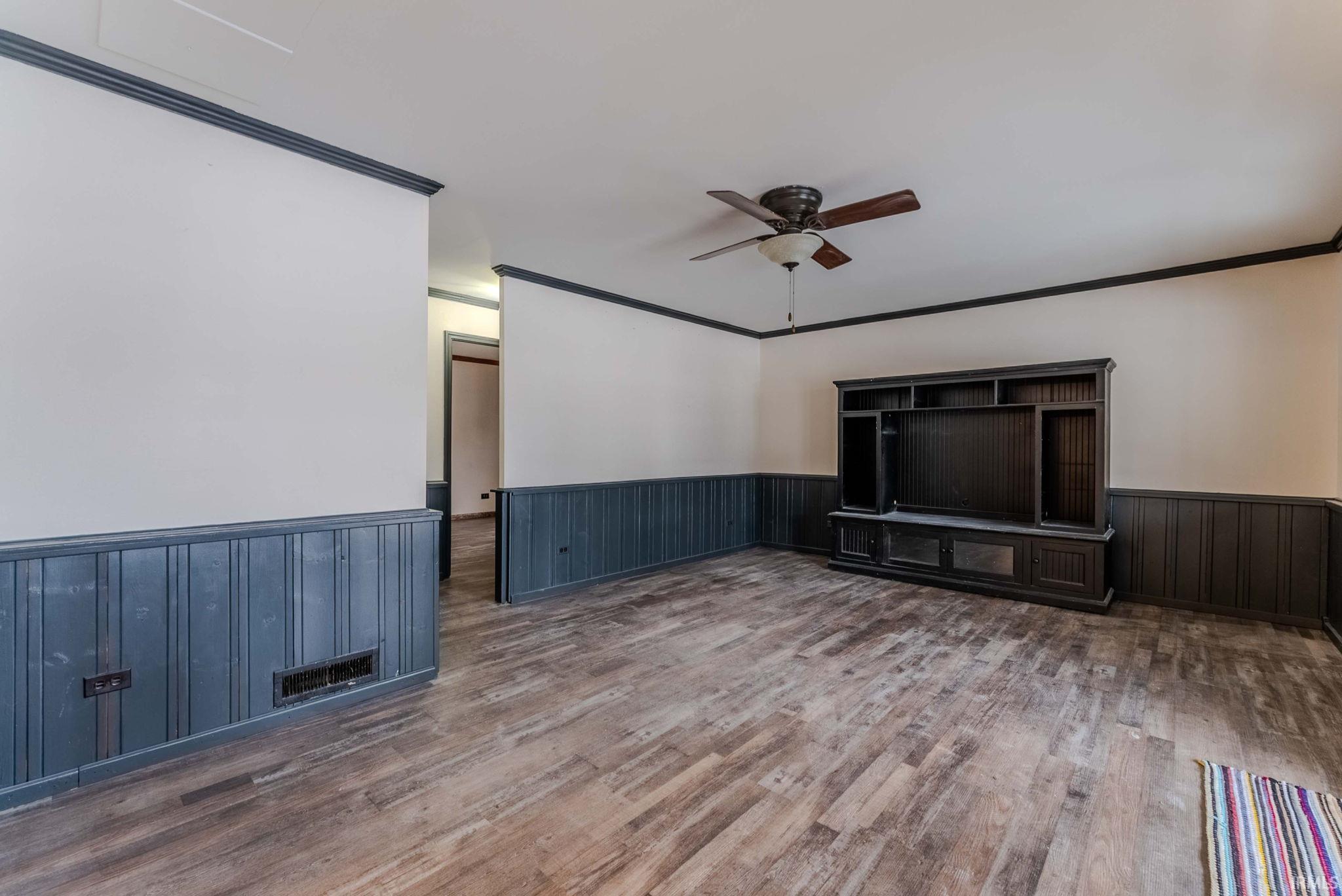 Unfurnished living room with ornamental molding, wainscoting, a ceiling fan, and dark wood-type flooring