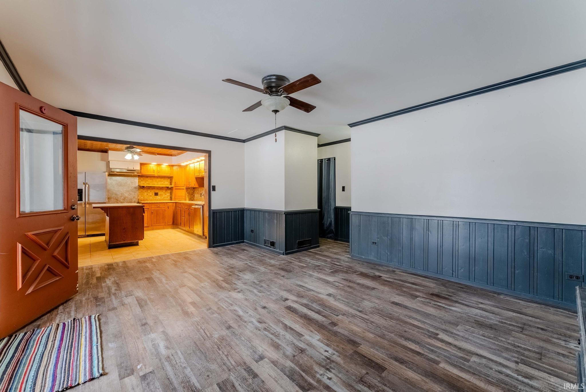 Unfurnished living room with wainscoting, a ceiling fan, and light wood finished floors
