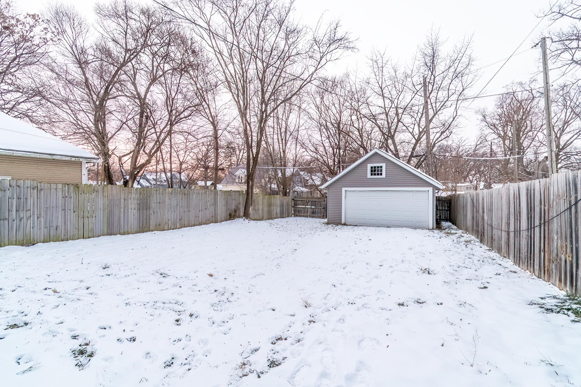 Yard layered in snow with a fenced backyard, an outbuilding, and a garage