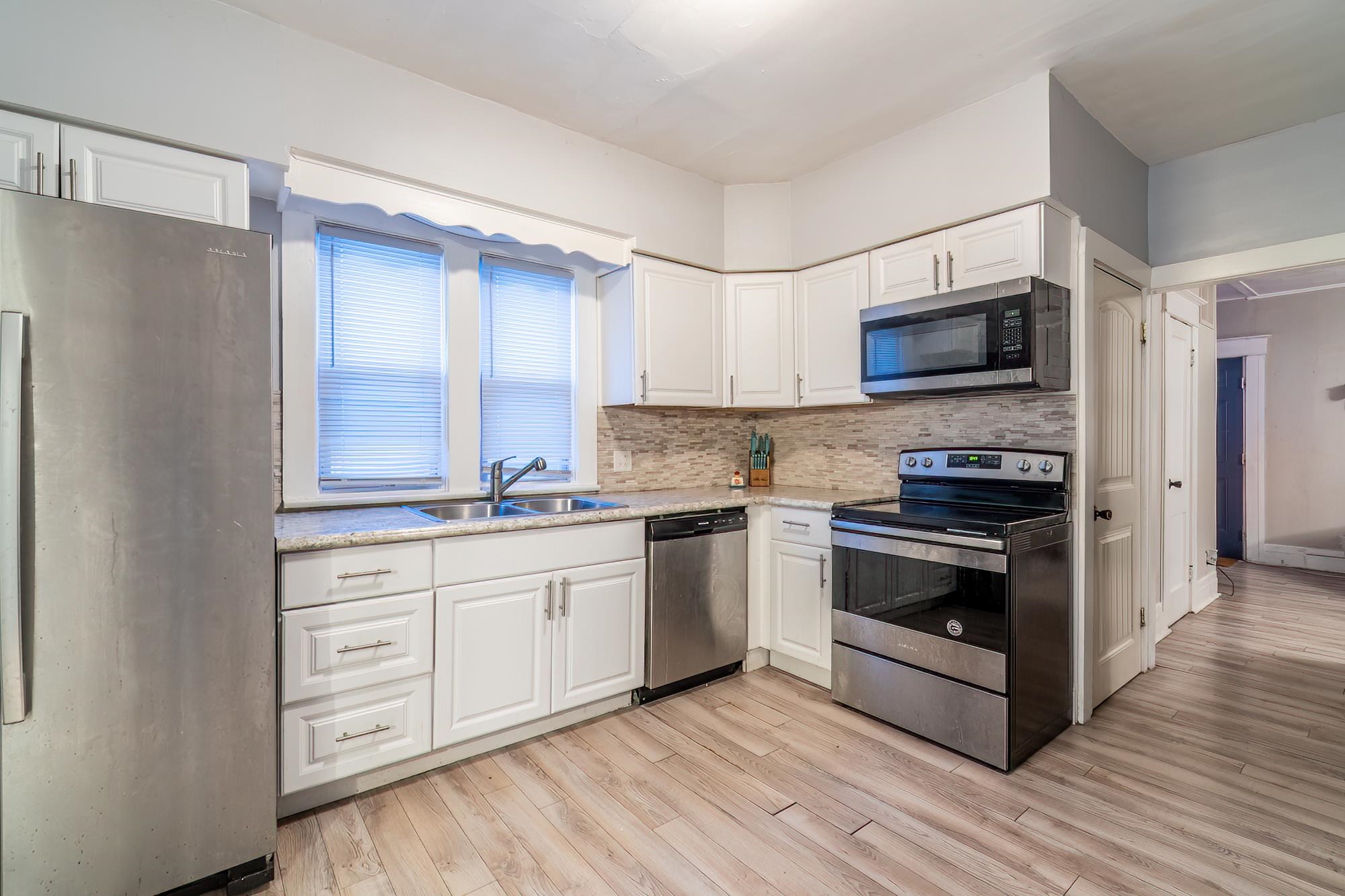 Kitchen with stainless steel appliances, white cabinetry, light wood-style flooring, and light stone countertops