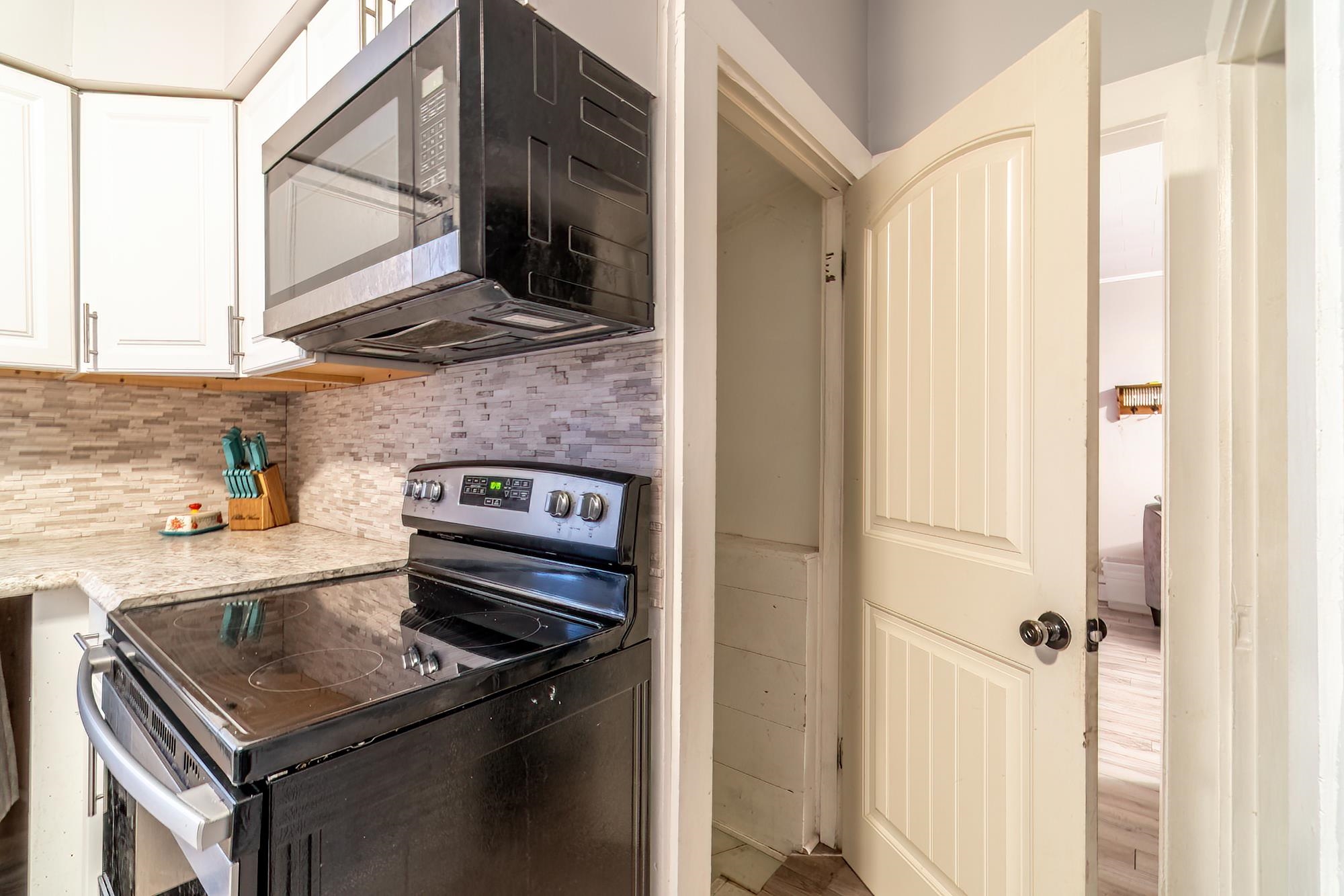 Kitchen with electric range oven, stainless steel microwave, white cabinets, light stone countertops, and backsplash
