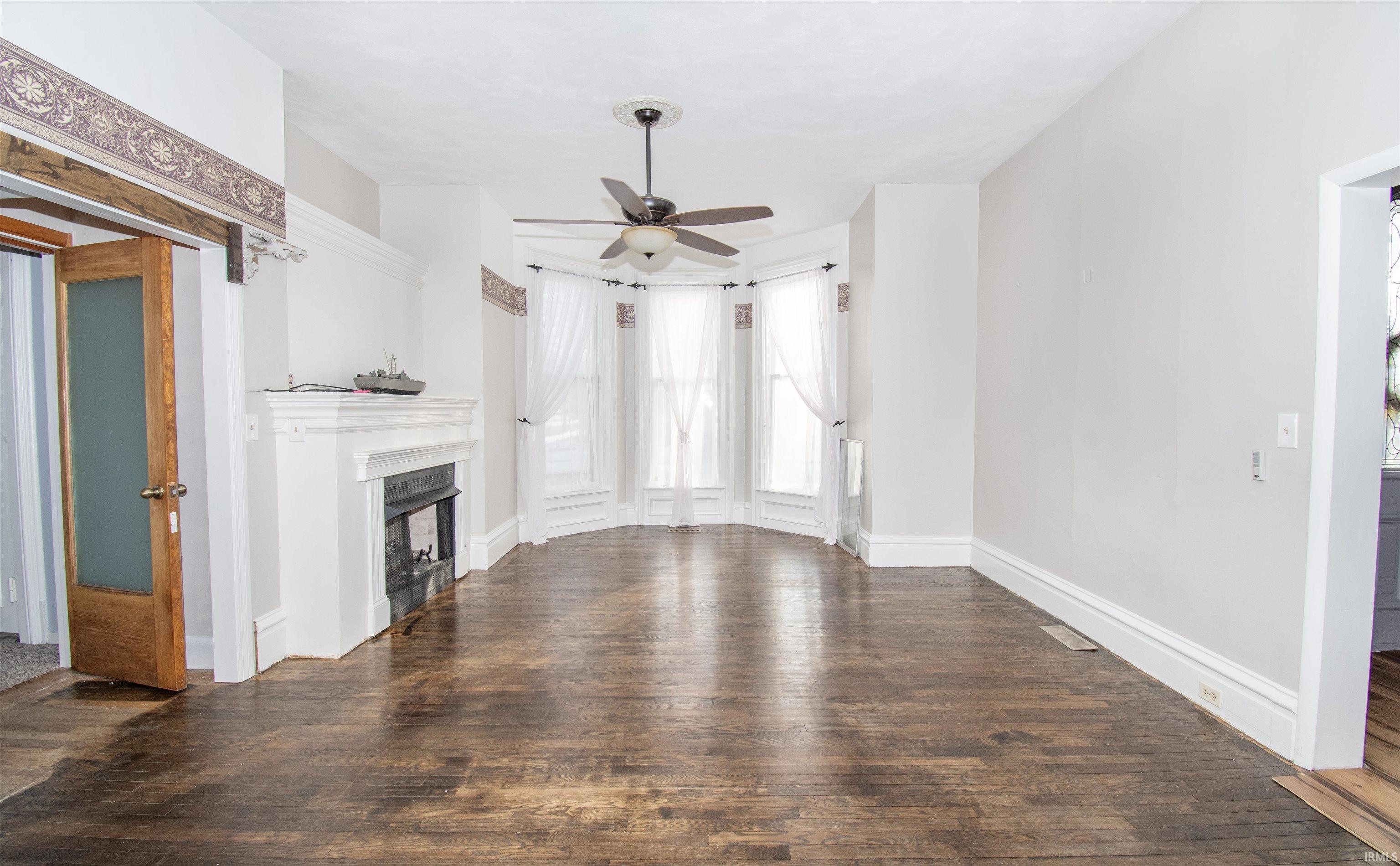 Unfurnished living room with dark wood-style floors, a fireplace, and a ceiling fan