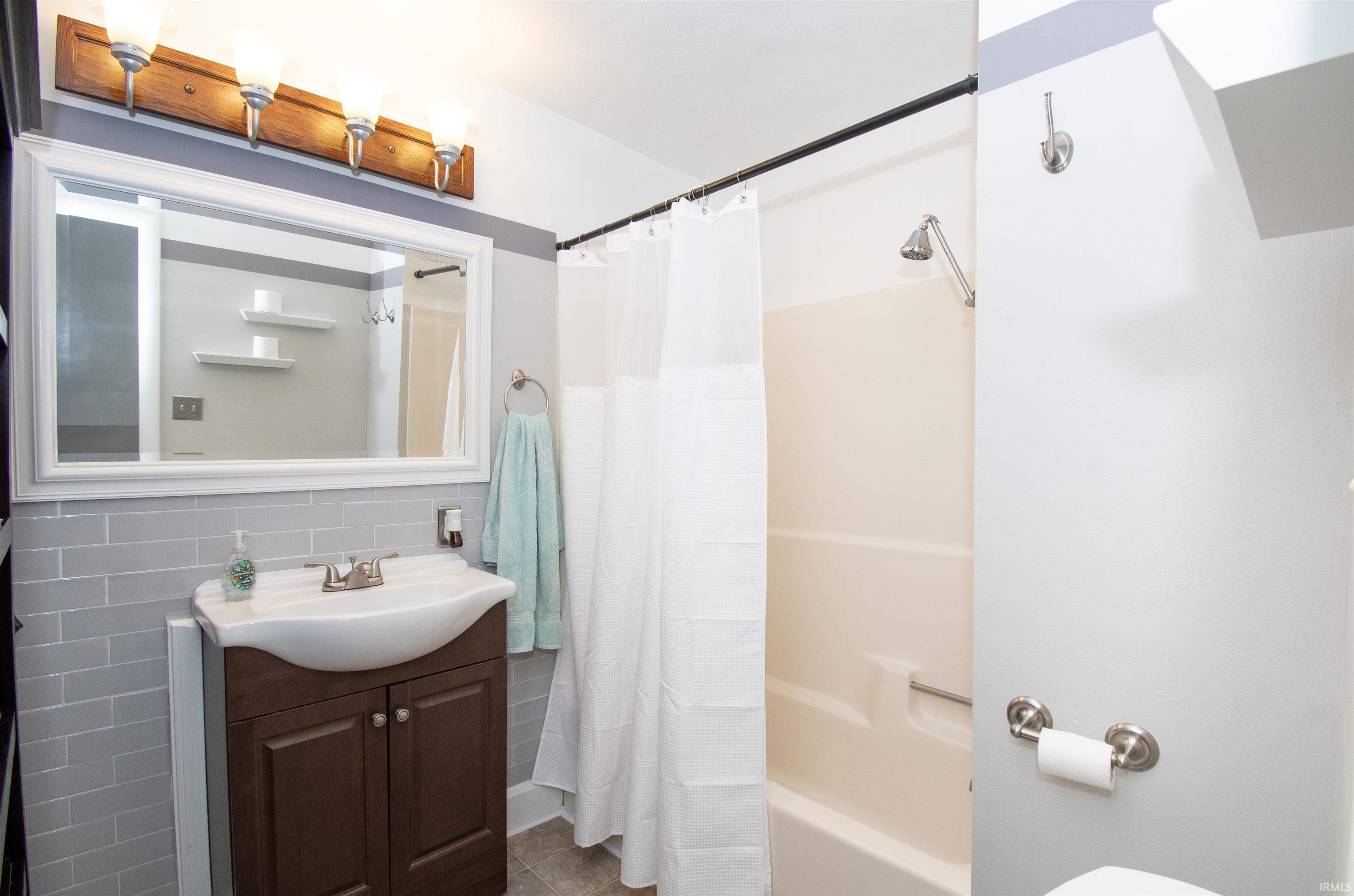 Bathroom with vanity, tile walls, and shower / bath combo with shower curtain
