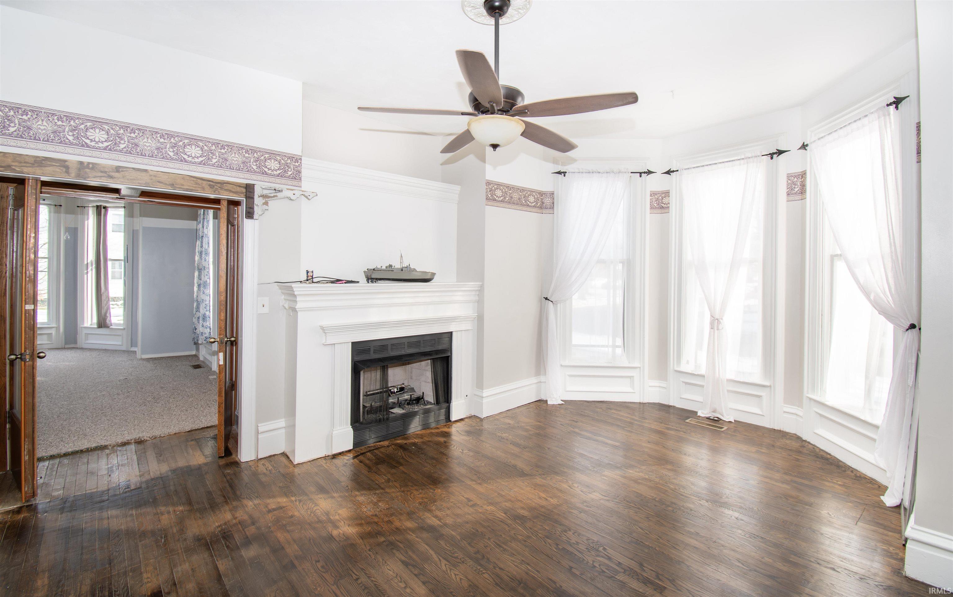 Unfurnished living room with a fireplace, dark wood-style flooring, and a ceiling fan