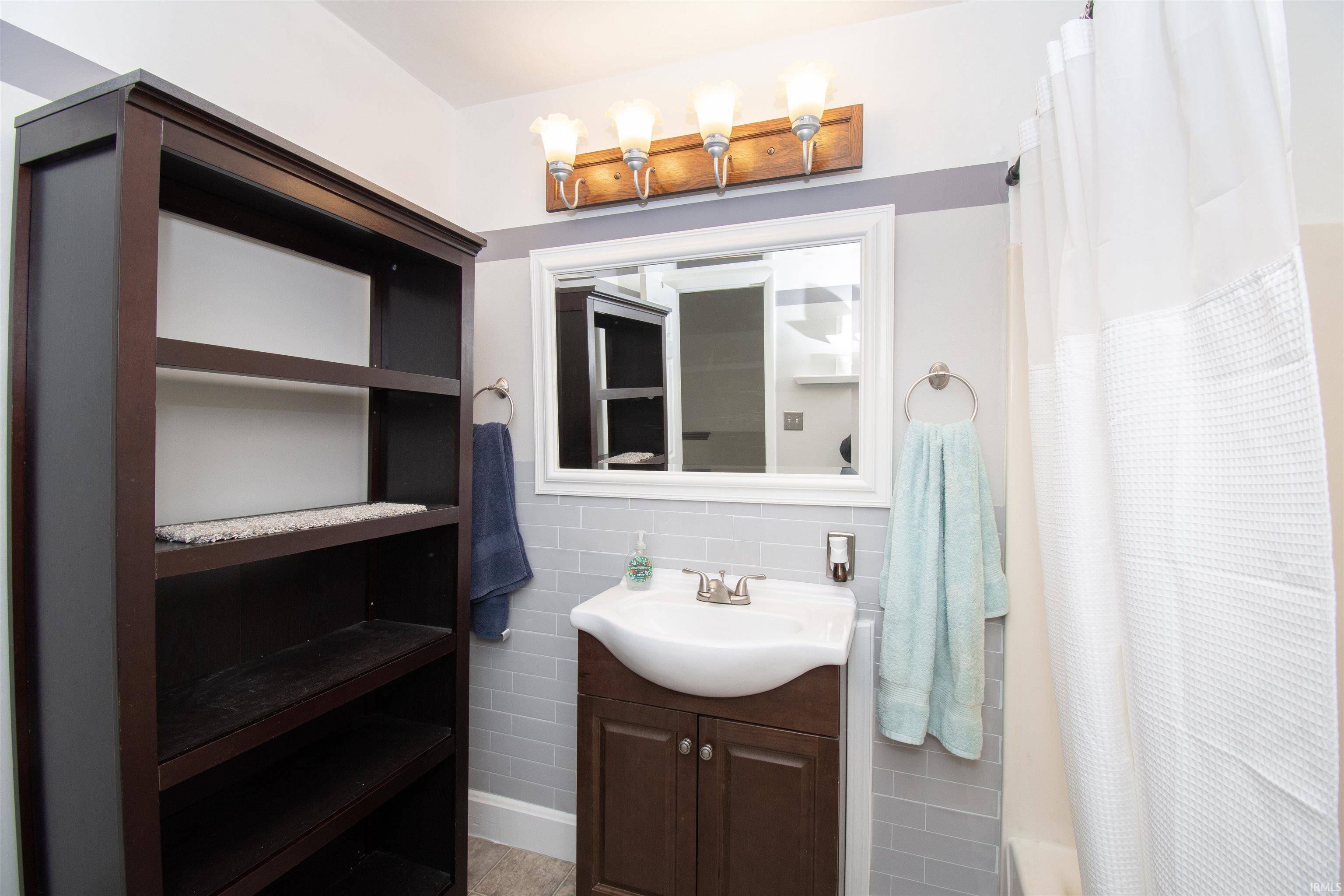 Full bath with tile walls, vanity, and decorative backsplash
