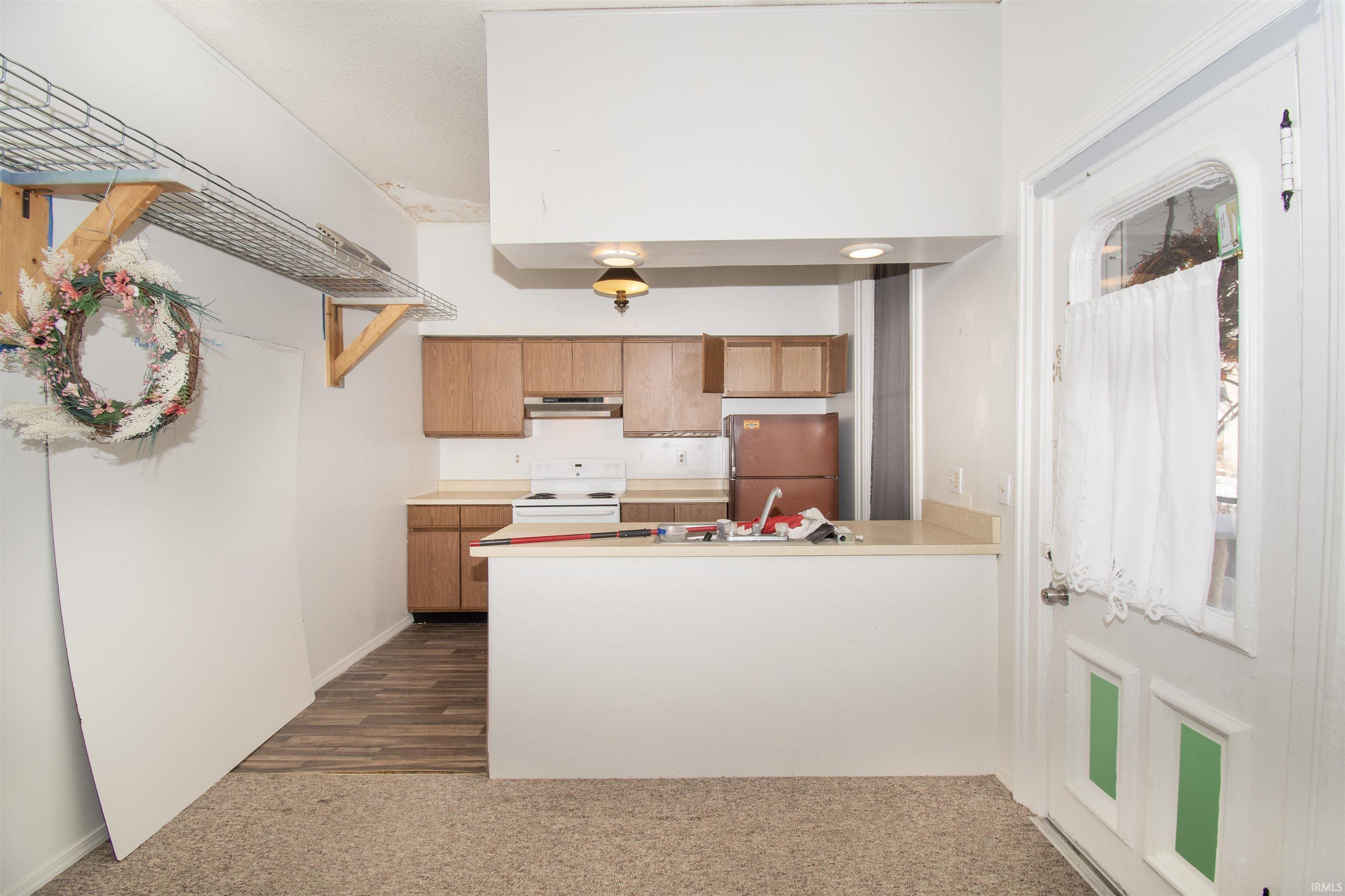 Kitchen with freestanding refrigerator, light countertops, white electric stove, and dark carpet