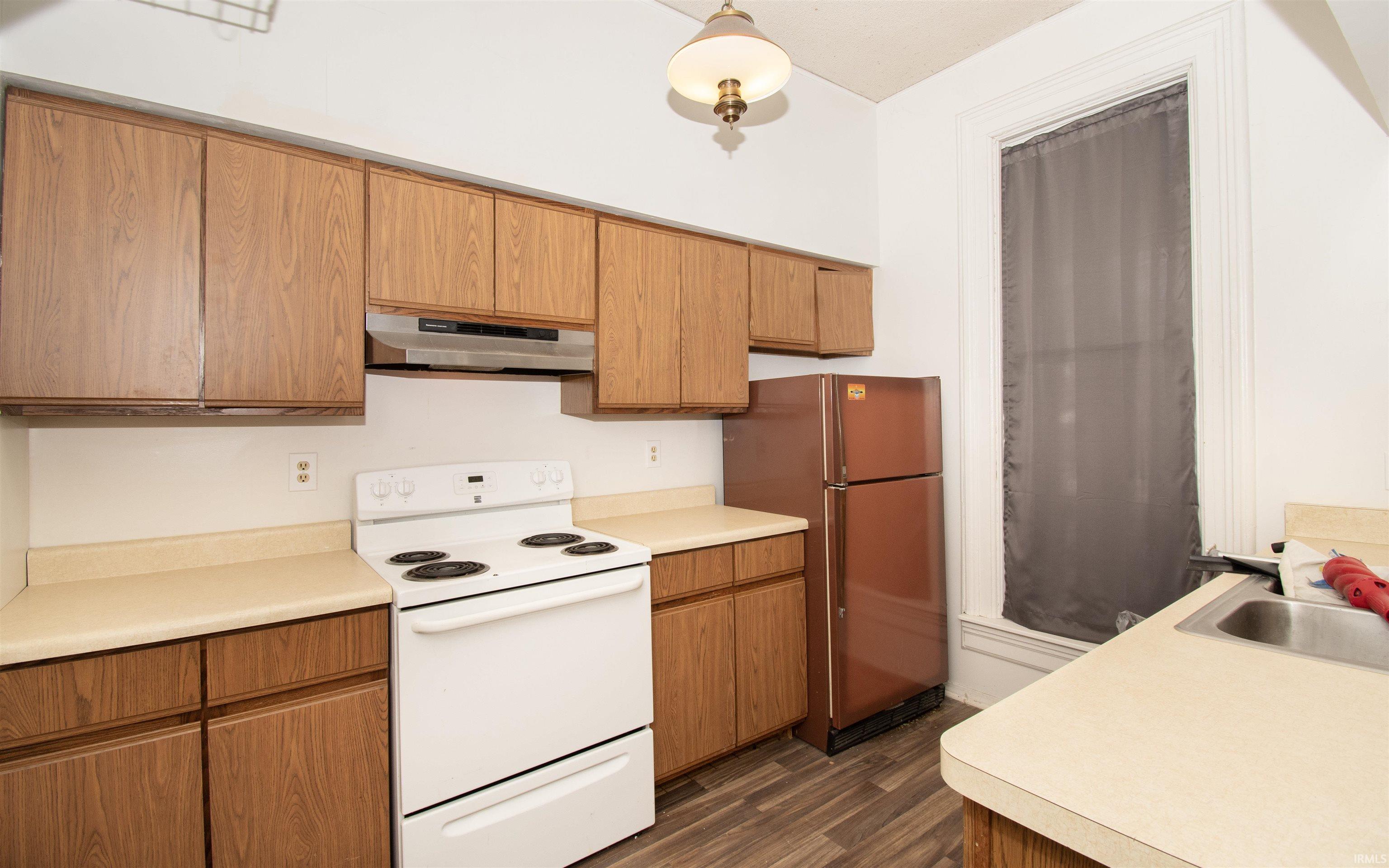 Kitchen featuring electric stove, freestanding refrigerator, light countertops, under cabinet range hood, and dark wood finished floors