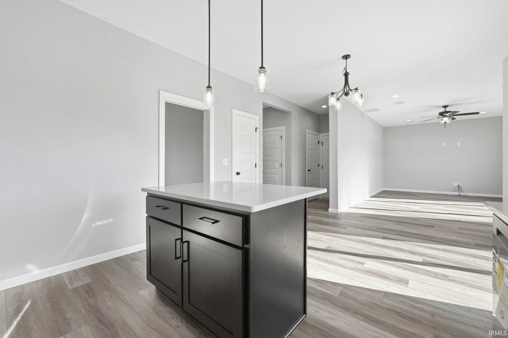 Kitchen with hanging light fixtures, a center island, light wood finished floors, open floor plan, and light stone countertops