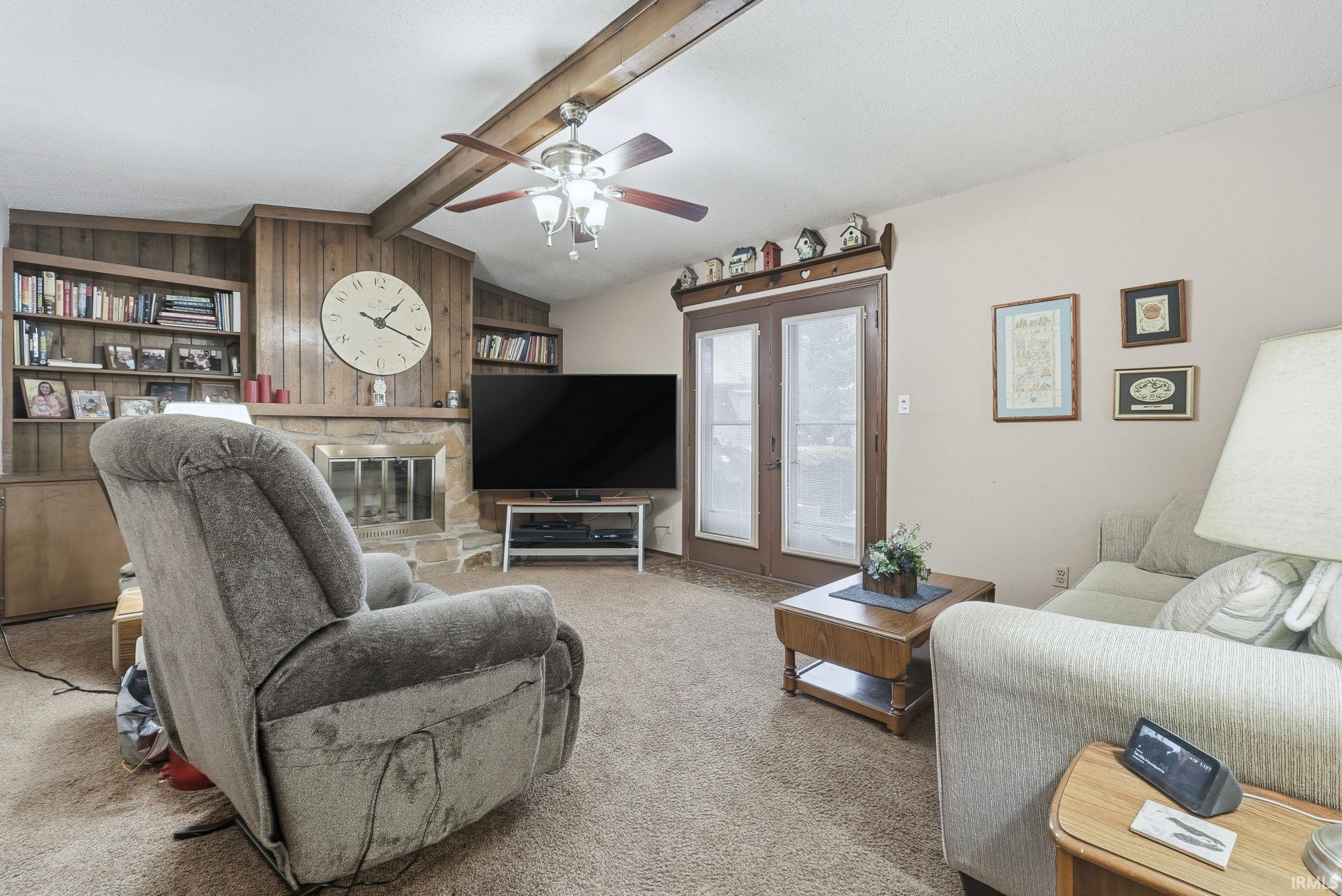 Living area with a stone fireplace, carpet, french doors, and ceiling fan