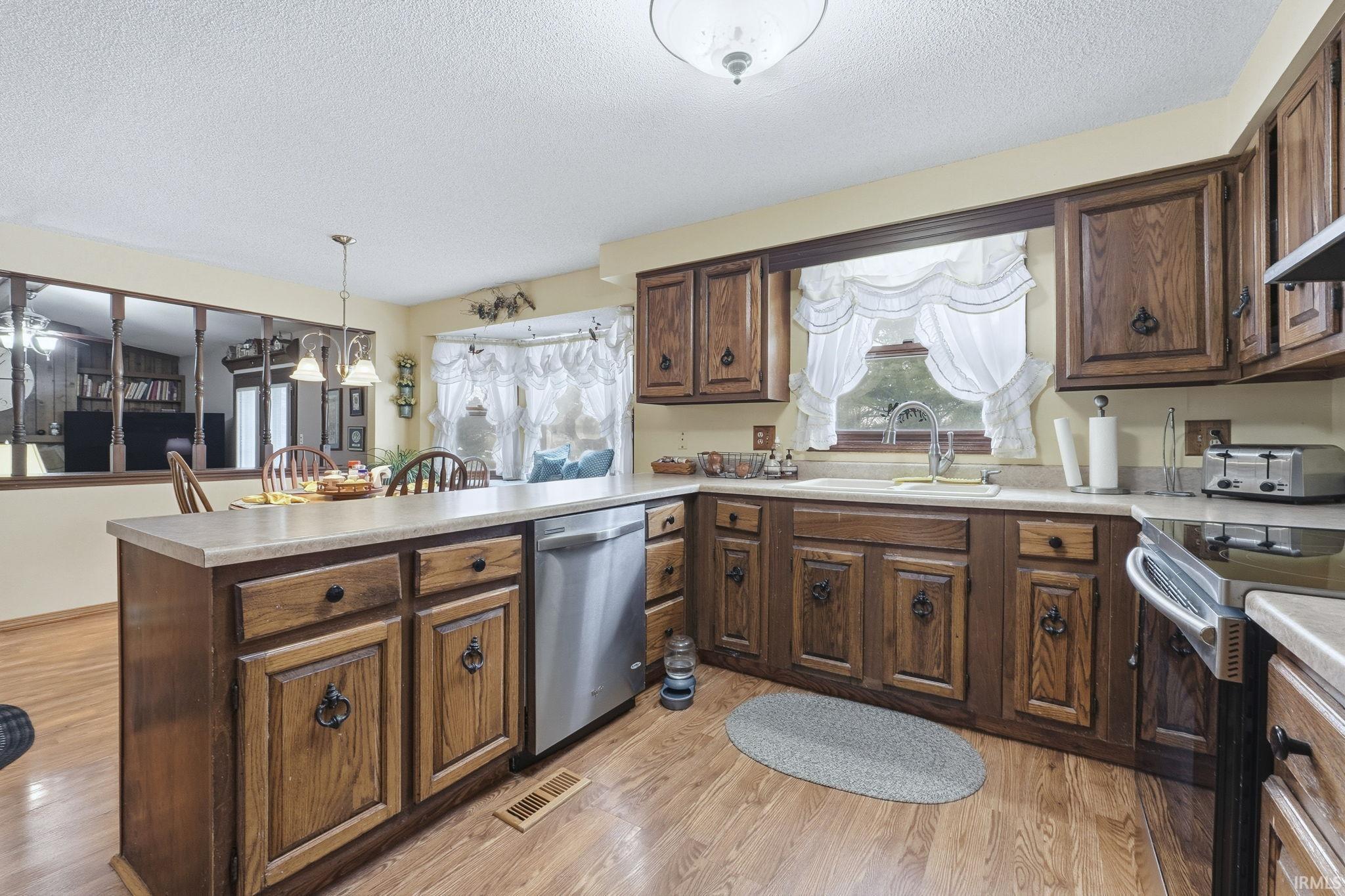 Kitchen featuring dark brown cabinetry, a textured ceiling, appliances with stainless steel finishes, a peninsula, and pendant lighting