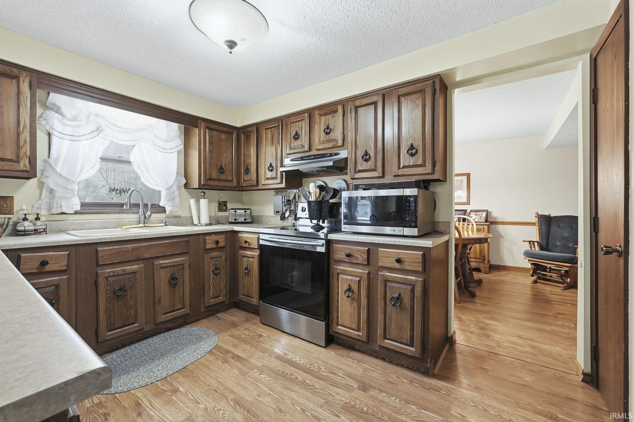 Kitchen with appliances with stainless steel finishes, light wood-style floors, light countertops, dark brown cabinetry, and under cabinet range hood