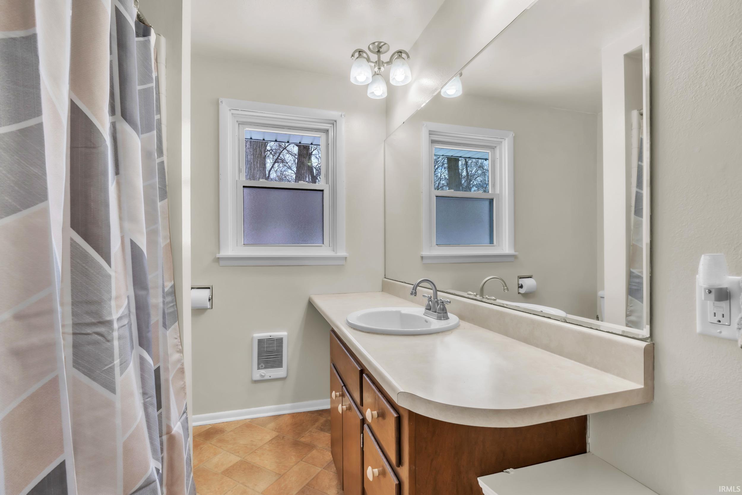 Full bathroom with vanity, curtained shower, heating unit, and a chandelier