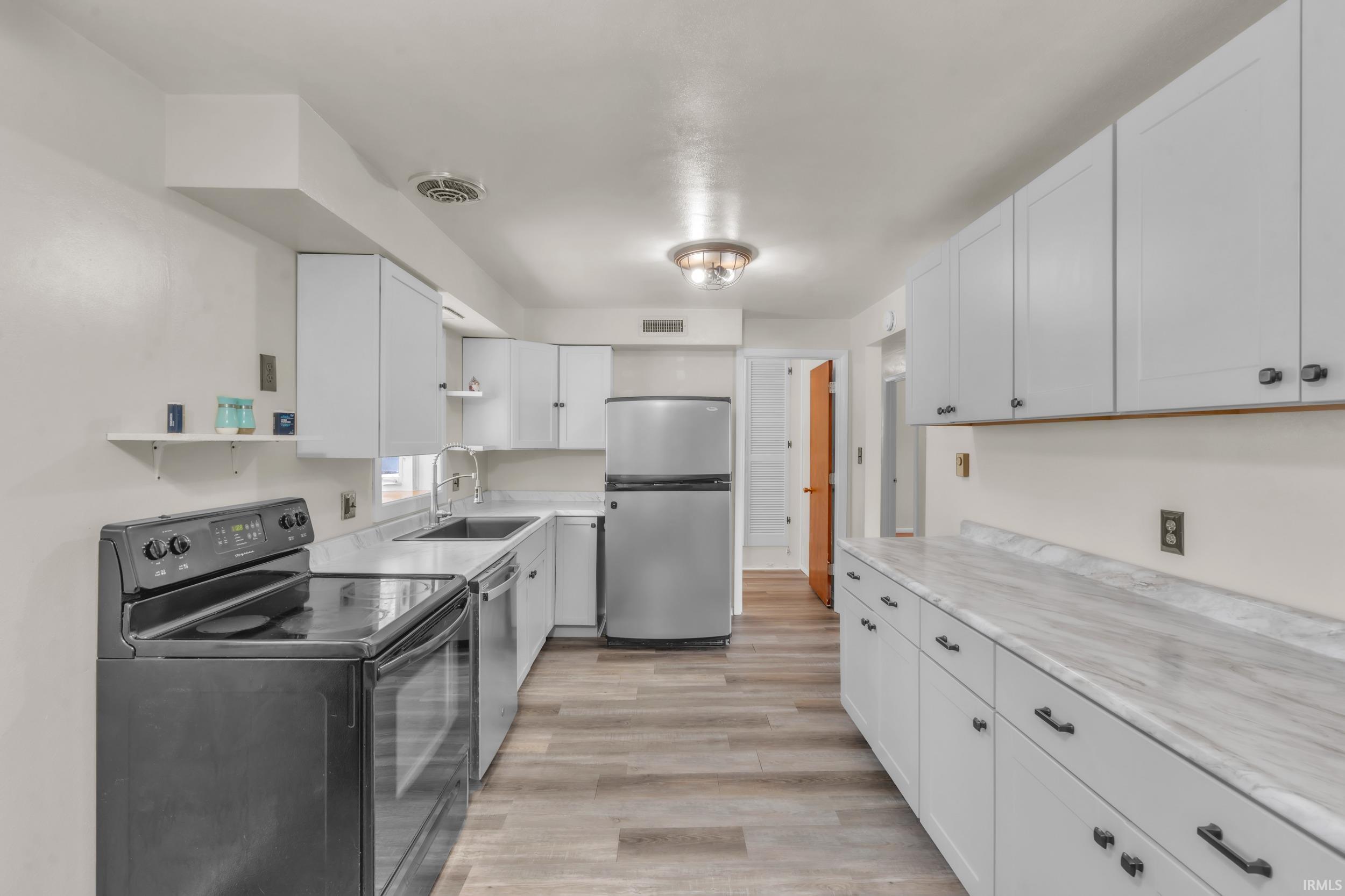 Kitchen with stainless steel appliances, light countertops, white cabinetry, and open shelves