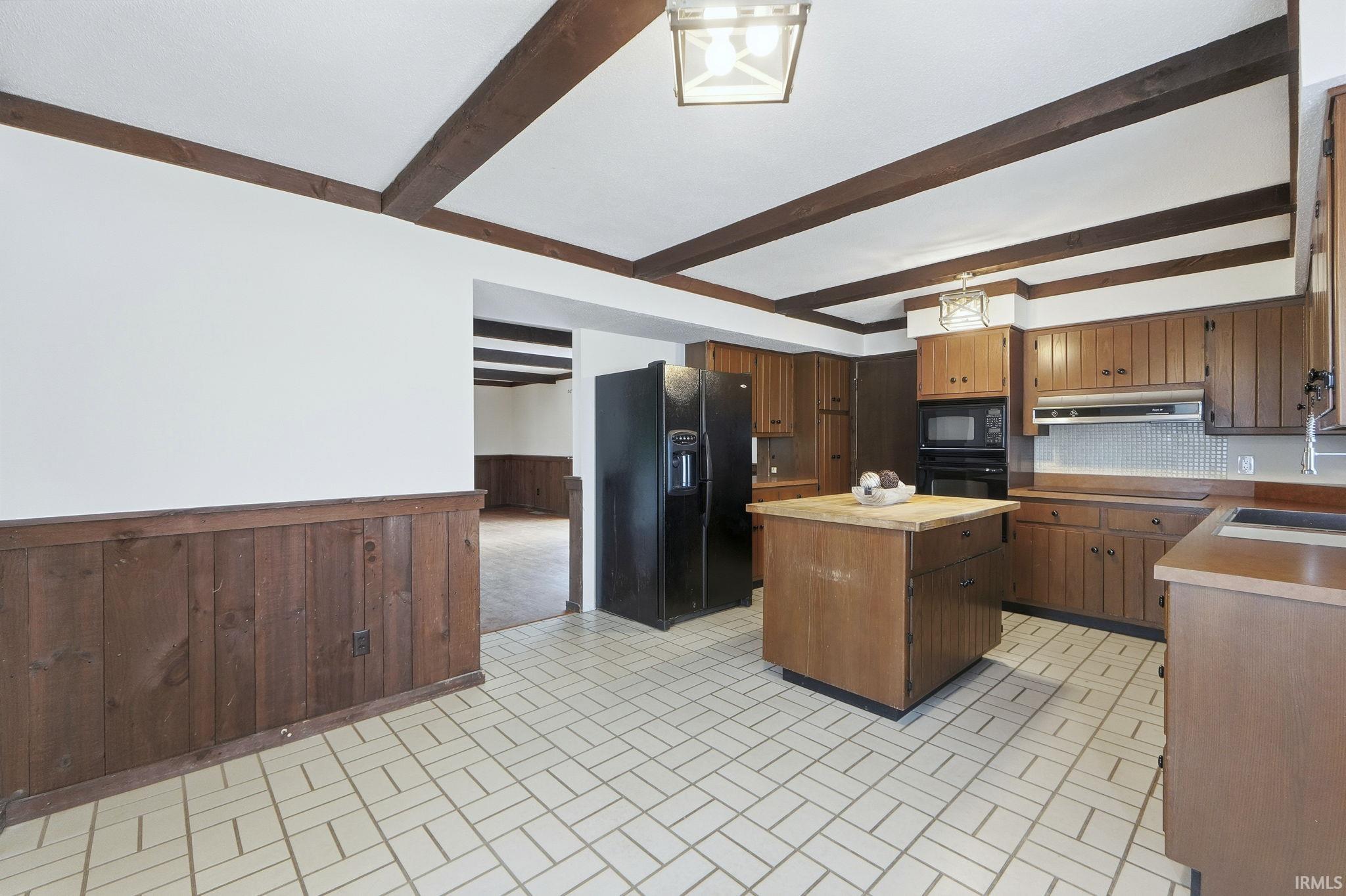 Kitchen featuring wainscoting, a center island, brick patterned floors, black appliances, and wooden walls
