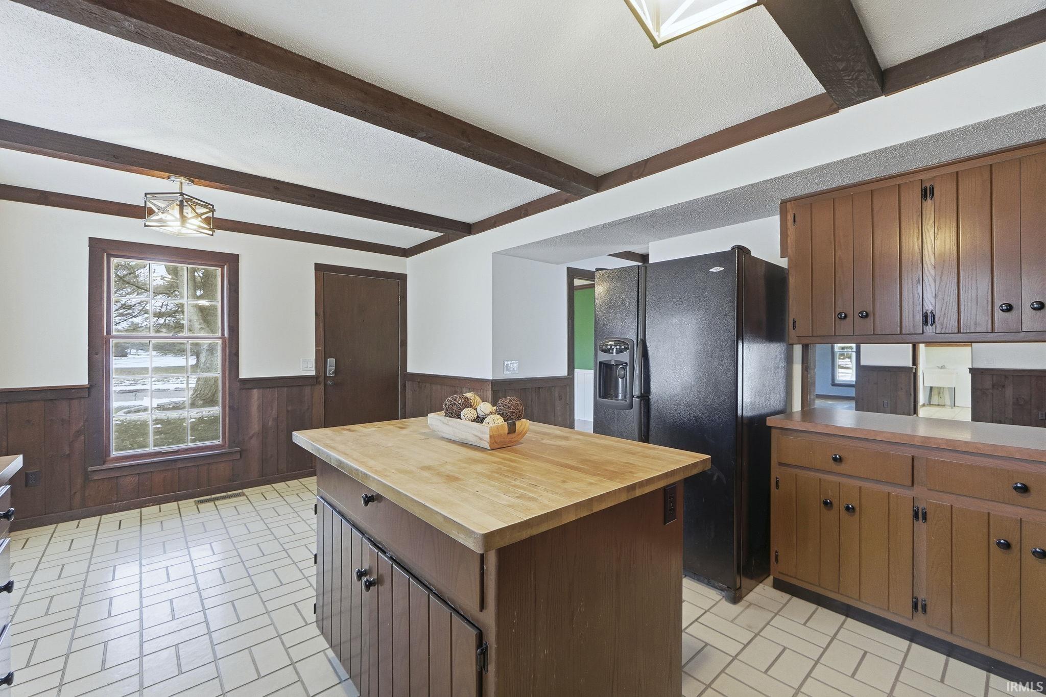 Kitchen featuring healthy amount of natural light, black fridge, a wainscoted wall, brick patterned floors, and a center island