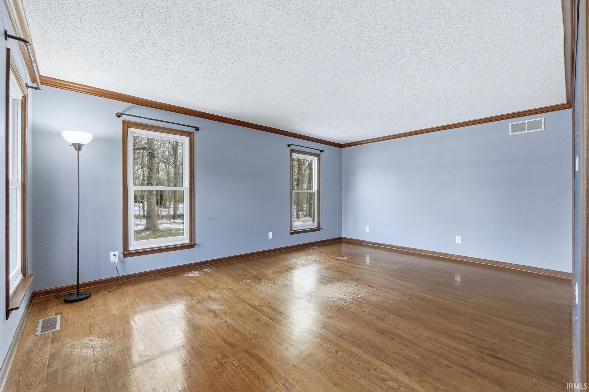 Empty room with a textured ceiling, crown molding, and wood-type flooring