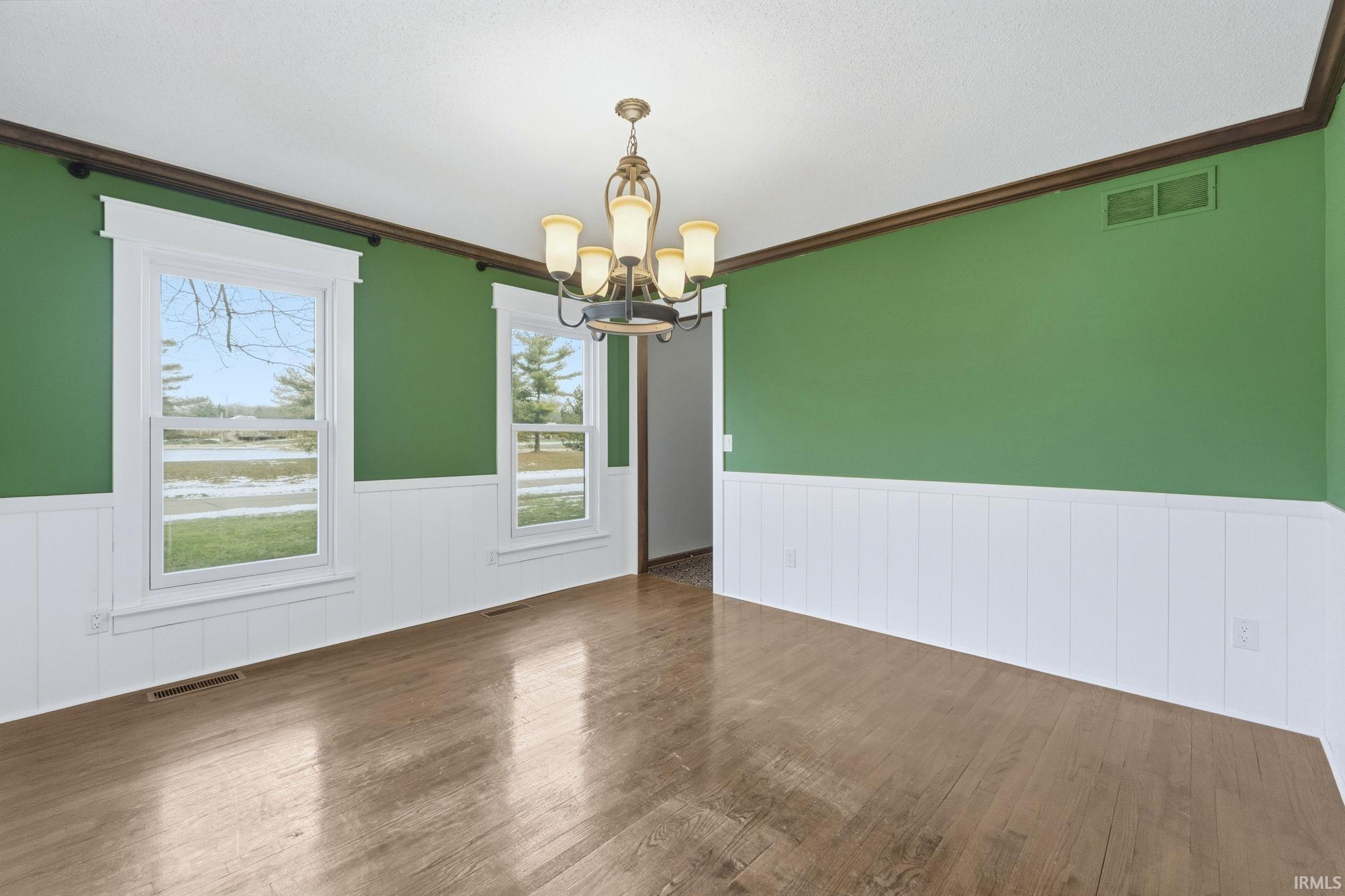 Unfurnished dining area with hardwood / wood-style floors, a chandelier, wainscoting, and ornamental molding