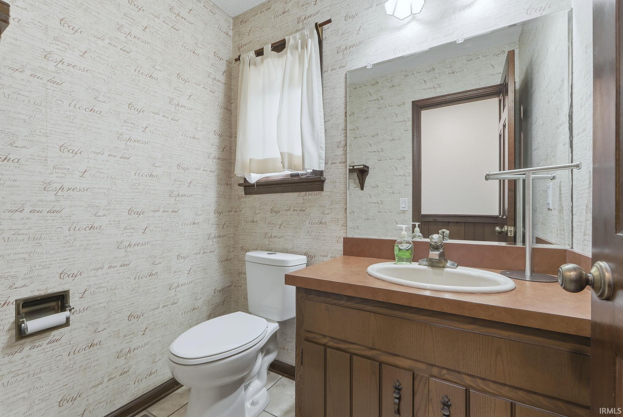Bathroom with wallpapered walls, vanity, and light tile patterned flooring