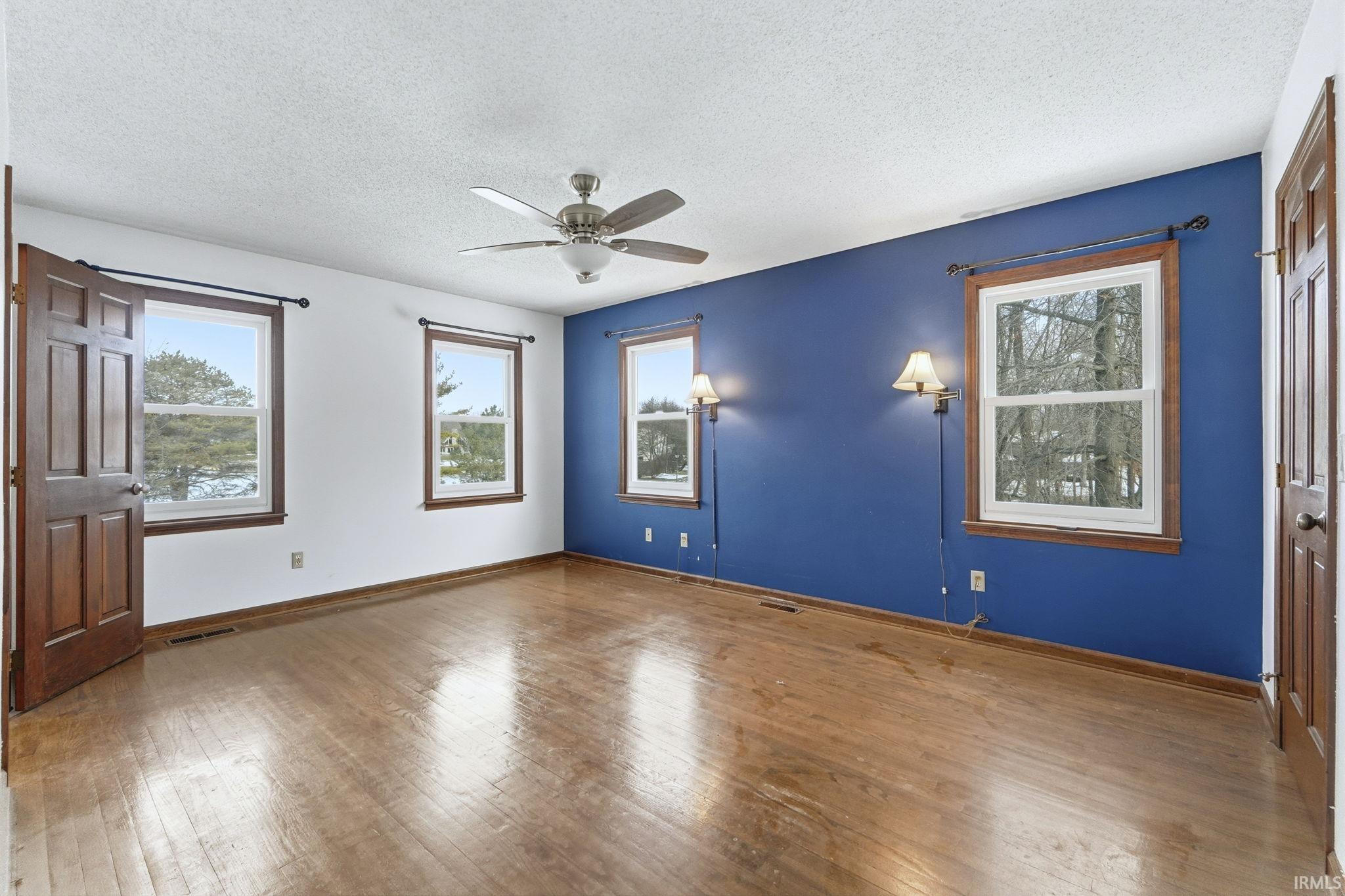 Unfurnished bedroom featuring hardwood / wood-style flooring, multiple windows, a textured ceiling, ceiling fan, and a closet
