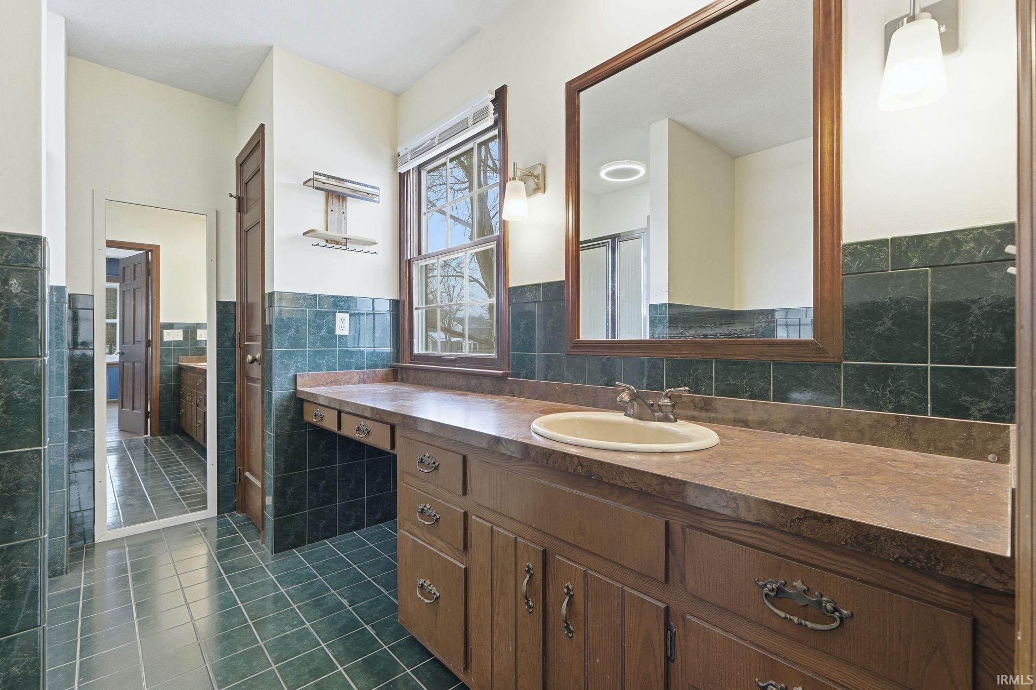 Full bathroom featuring dark tile patterned floors, vanity, wainscoting, tile walls, and a stall shower