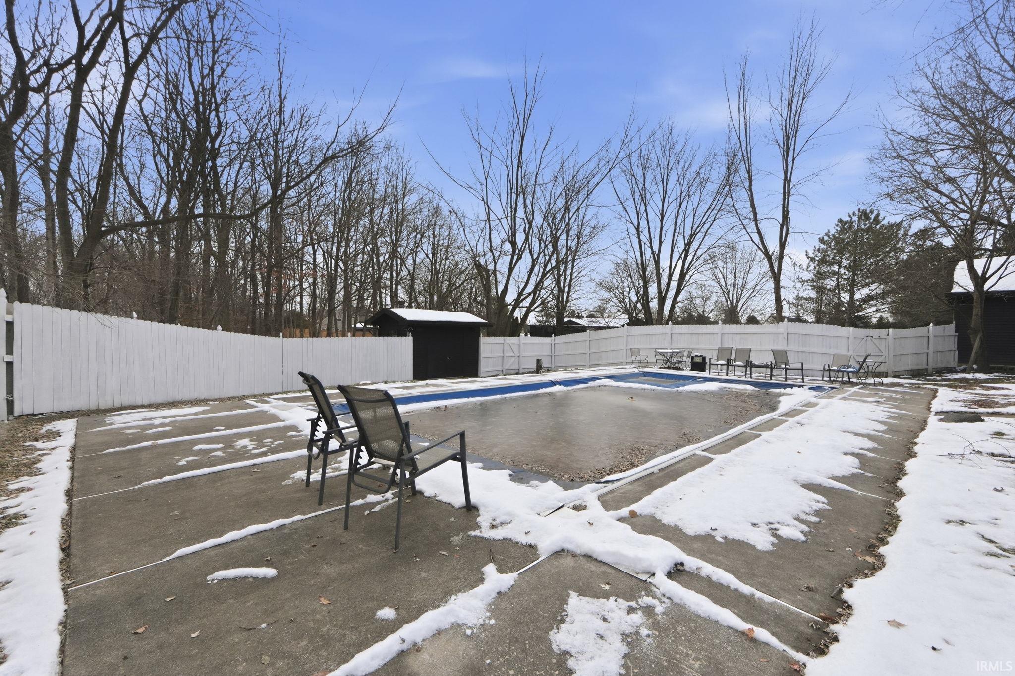 Snow covered pool with a fenced backyard, a patio area, and an outdoor structure