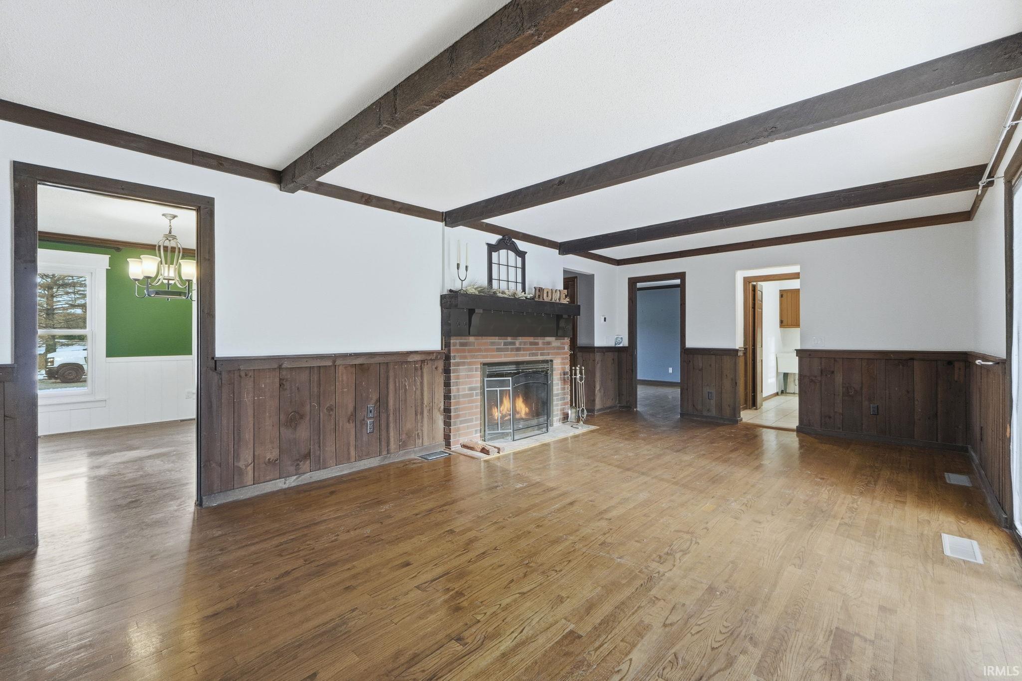 Unfurnished living room with wainscoting, wood-type flooring, a brick fireplace, and a chandelier