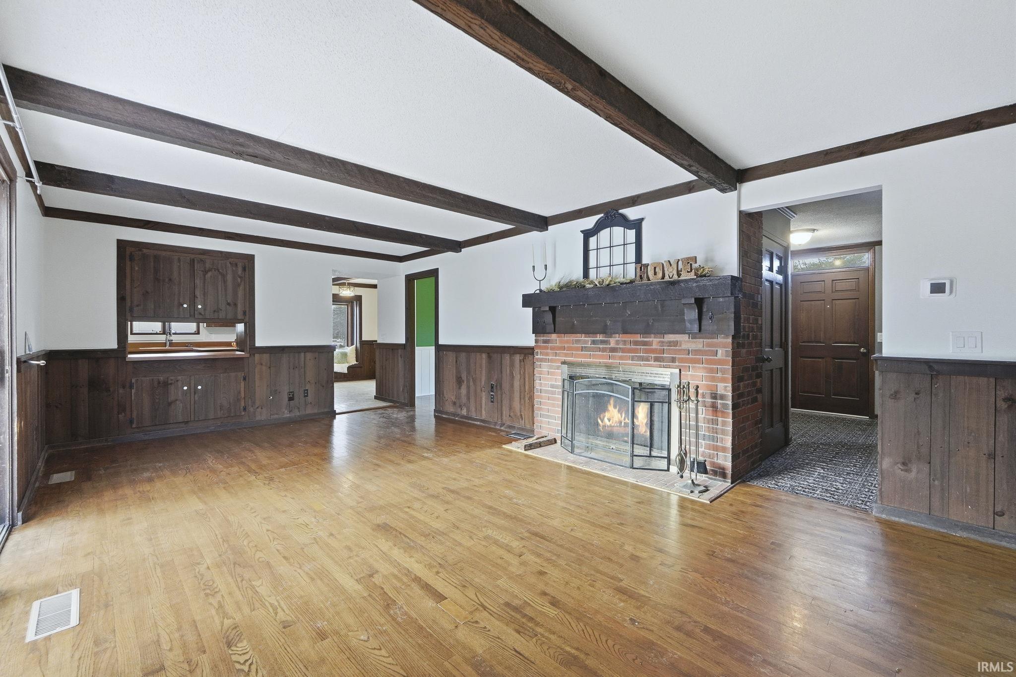 Unfurnished living room featuring wainscoting, wooden walls, a fireplace, wood finished floors, and plenty of natural light