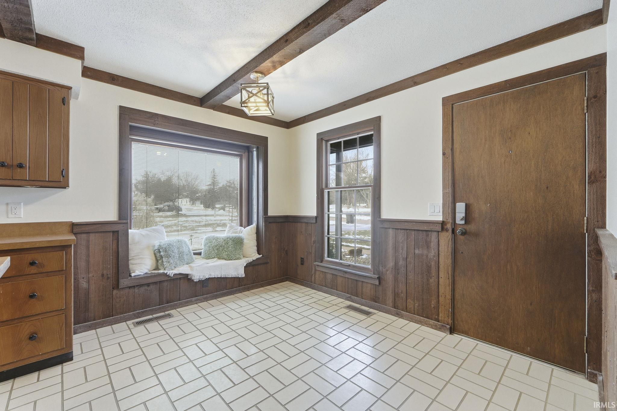 Unfurnished dining area with brick patterned flooring, wood walls, beamed ceiling, a wainscoted wall, and a textured ceiling